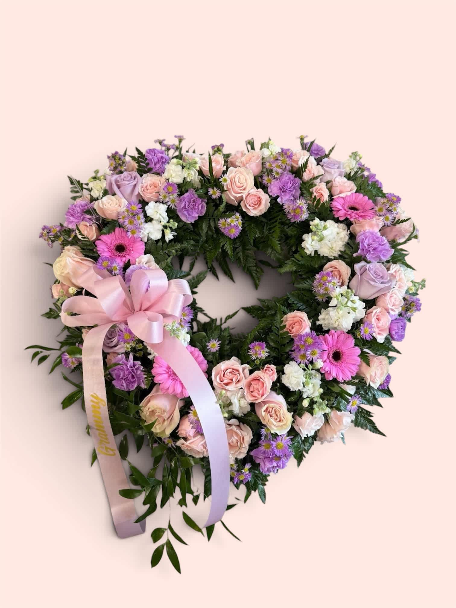 Heart-shaped floral wreath with pink, purple, and white flowers and a satin ribbon