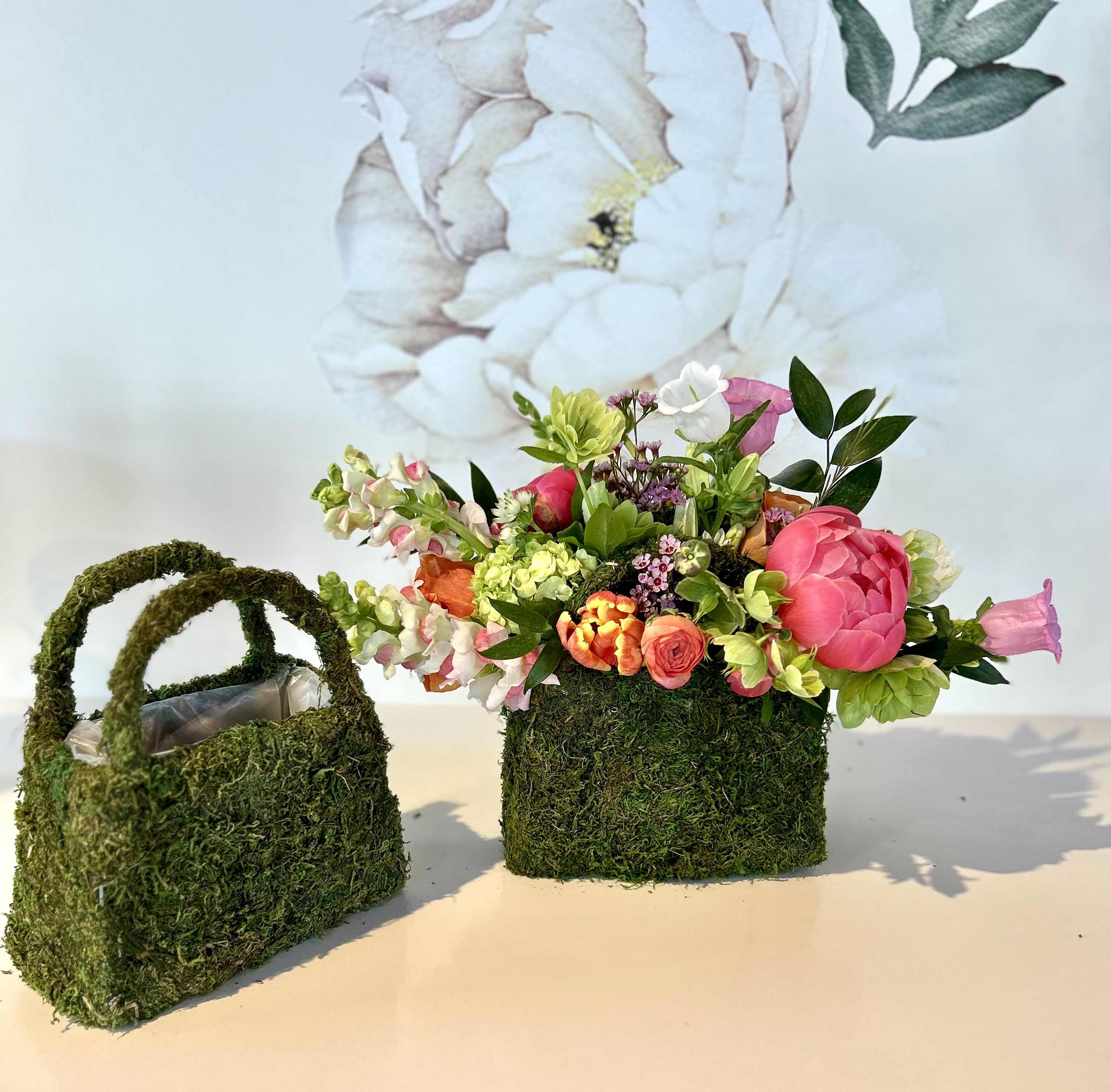 Flower arrangement in a moss-covered handbag-shaped container with pink and white blooms