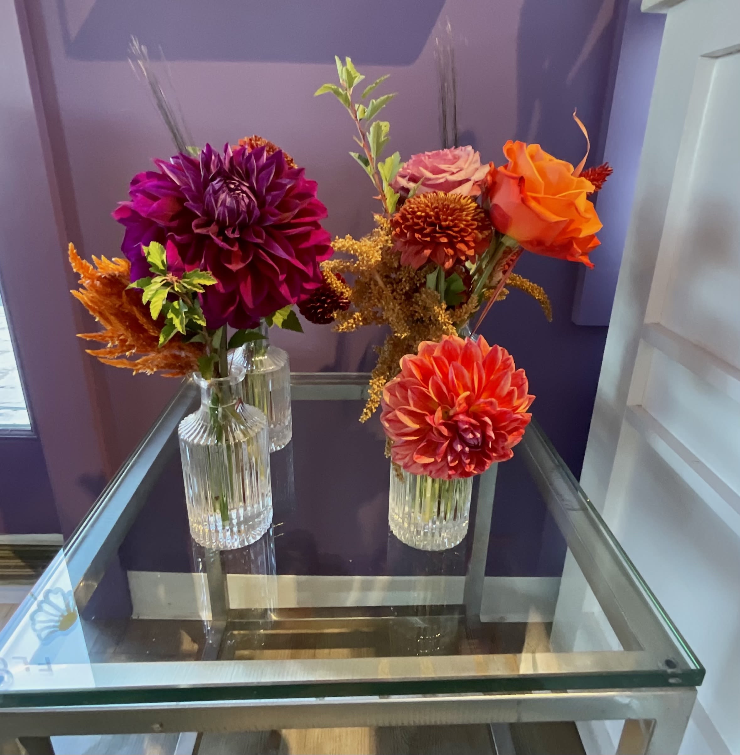 Three small floral arrangements in clear glass vases on a glass table