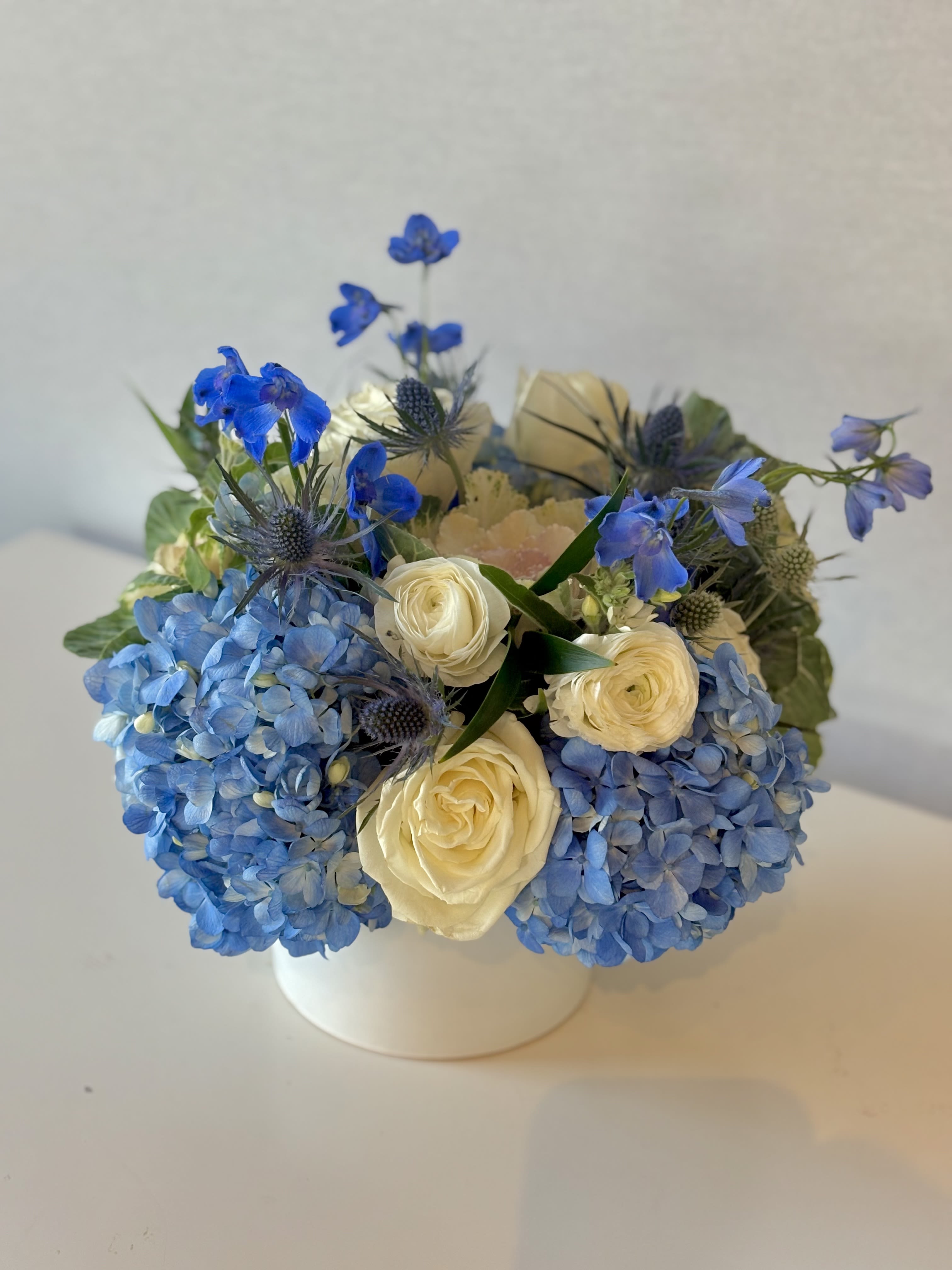 Blue hydrangeas and cream roses arranged in a white vase