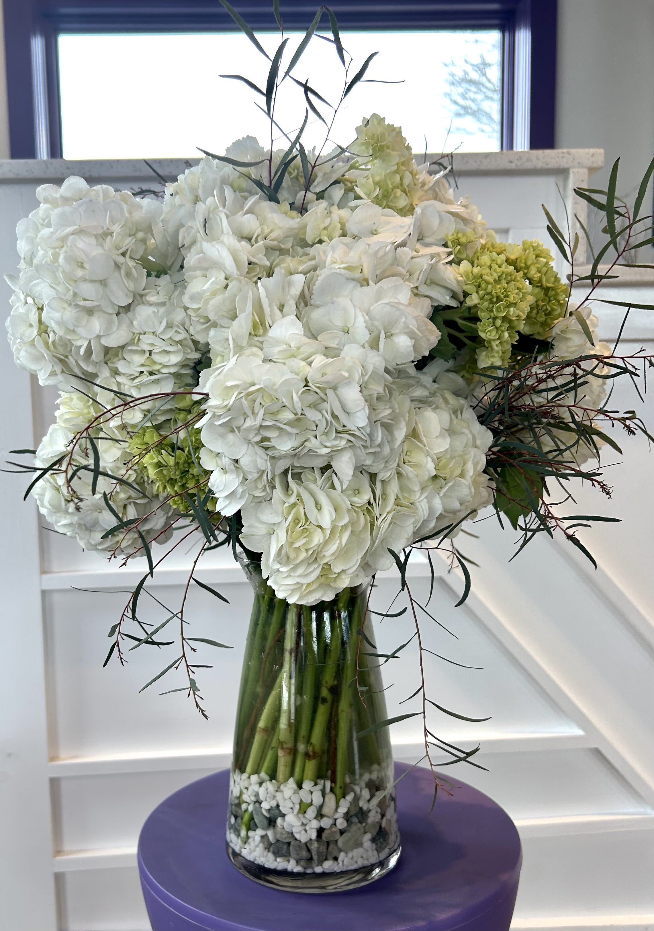 White hydrangea arrangement in a glass vase with pebbles