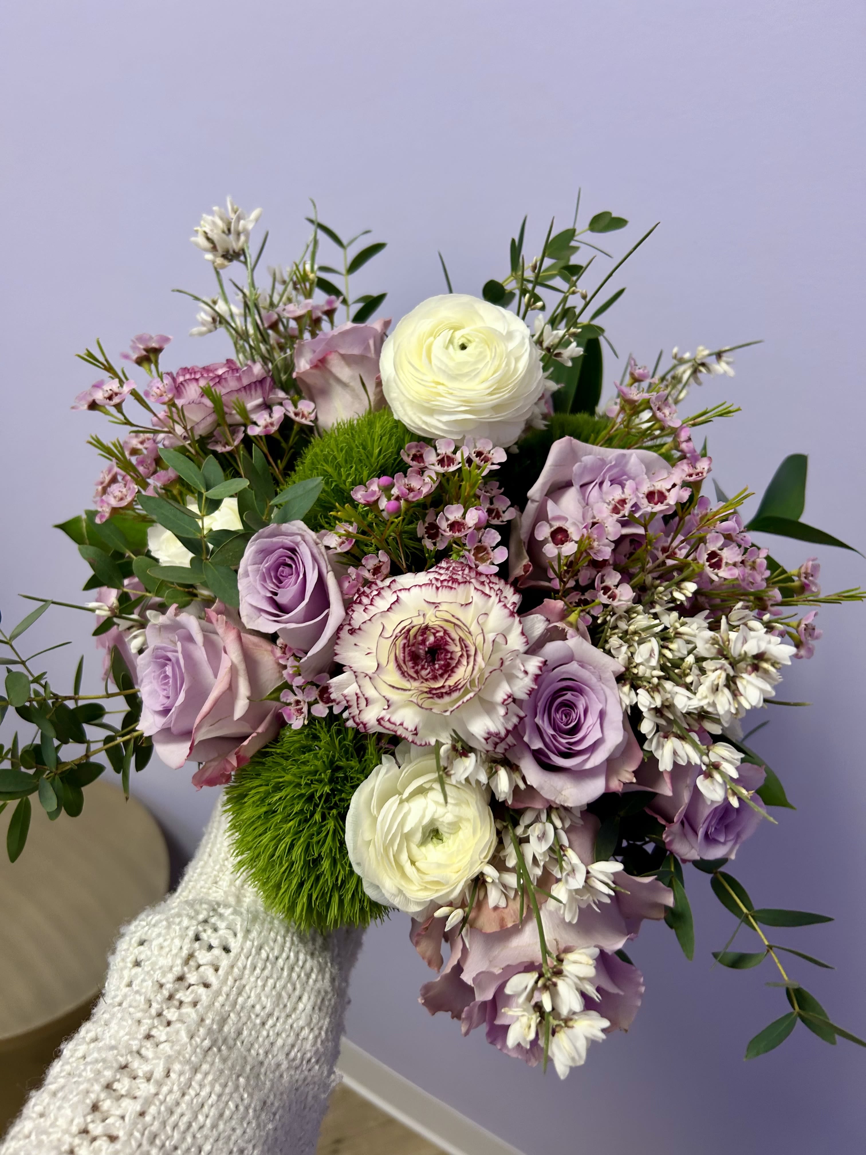 Handheld bouquet of lavender roses, white ranunculus, and pink blooms