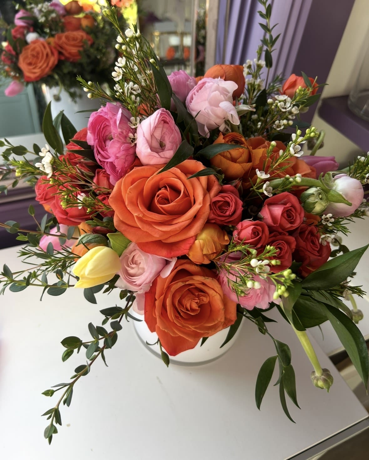 Mixed bouquet of orange, pink, and red roses in a white vase