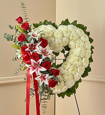 Red Rose and Lily Open Heart Standing Spray - The passing of someone we love deeply requires a special tribute. Our open heart standing arrangement of fresh white blooms, accented by red roses and Stargazer lilies cascading down one side and adorned with a red satin ribbon, will help you express the devotion and sympathy in your heart.  Our florists hand-design each arrangement, so colors and varieties may vary due to local availability Arrangement of roses, Stargazer lilies, mums, spiral and seeded eucalyptus and salal Arrangement measures approximately 28"H x 26"L without easel Appropriate to send to the funeral service