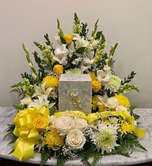 Yellow and white floral funeral arrangement with a gray urn centerpiece