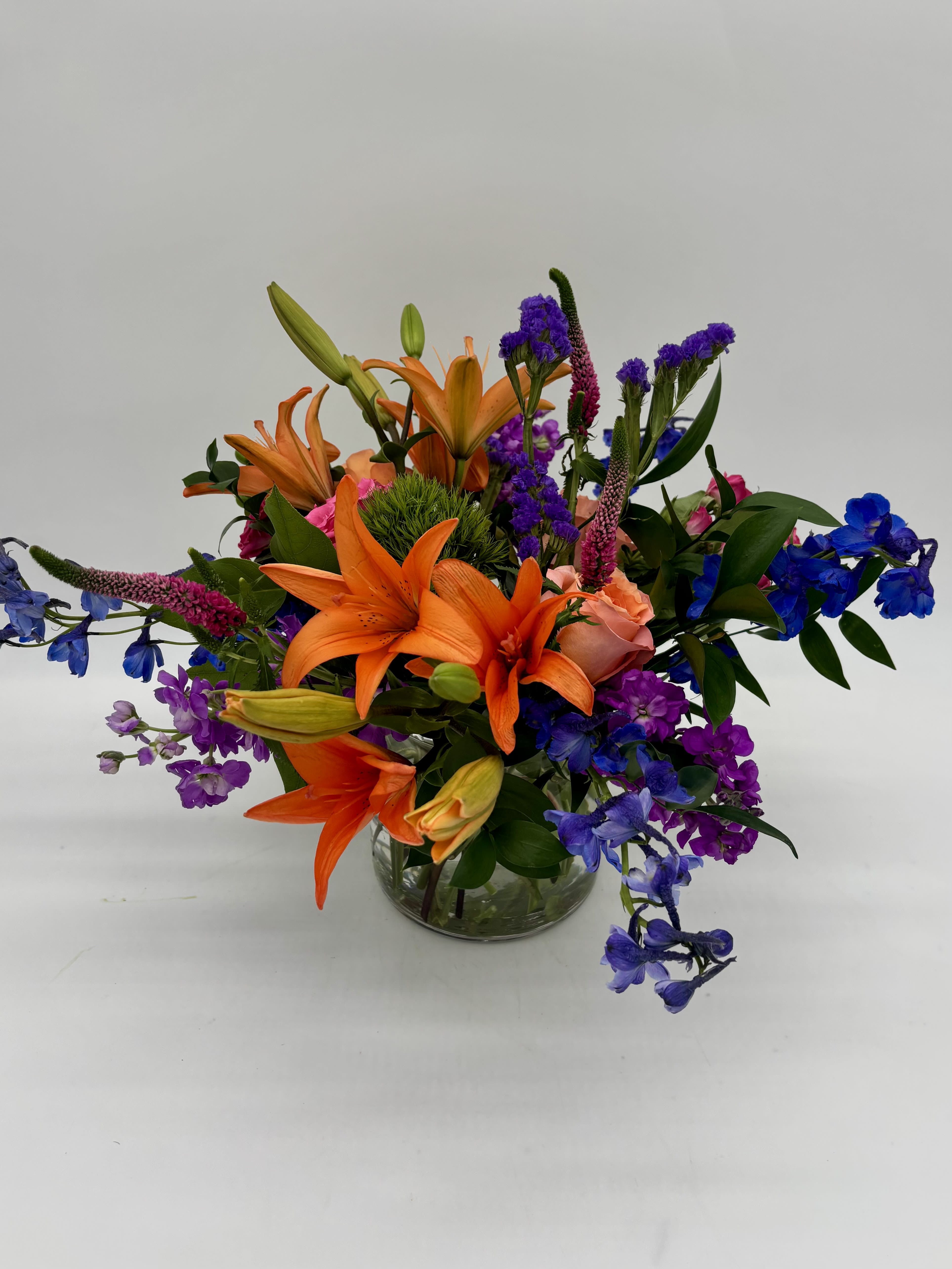 Breezy Meadows Bouquet - Bursting with exquisite colors and voluminous texture, the Breezy Meadows Bouquet brings the beauty of nature indoors, leaving your recipient feeling grounded and loved.  Details The Standard Bouquet is approximately 17"H x 20"W. Designed by florists, ready to display. For long–lasting blooms, replace the water daily. We suggest trimming the stems every couple days. Pet Safety Precautions: This bouquet or plant may include flowers and foliage that are known to be toxic to pets. To keep them safe, be sure to keep this arrangement out of your pet's reach.  Bloom Details Delphinium Rose Lily Stock