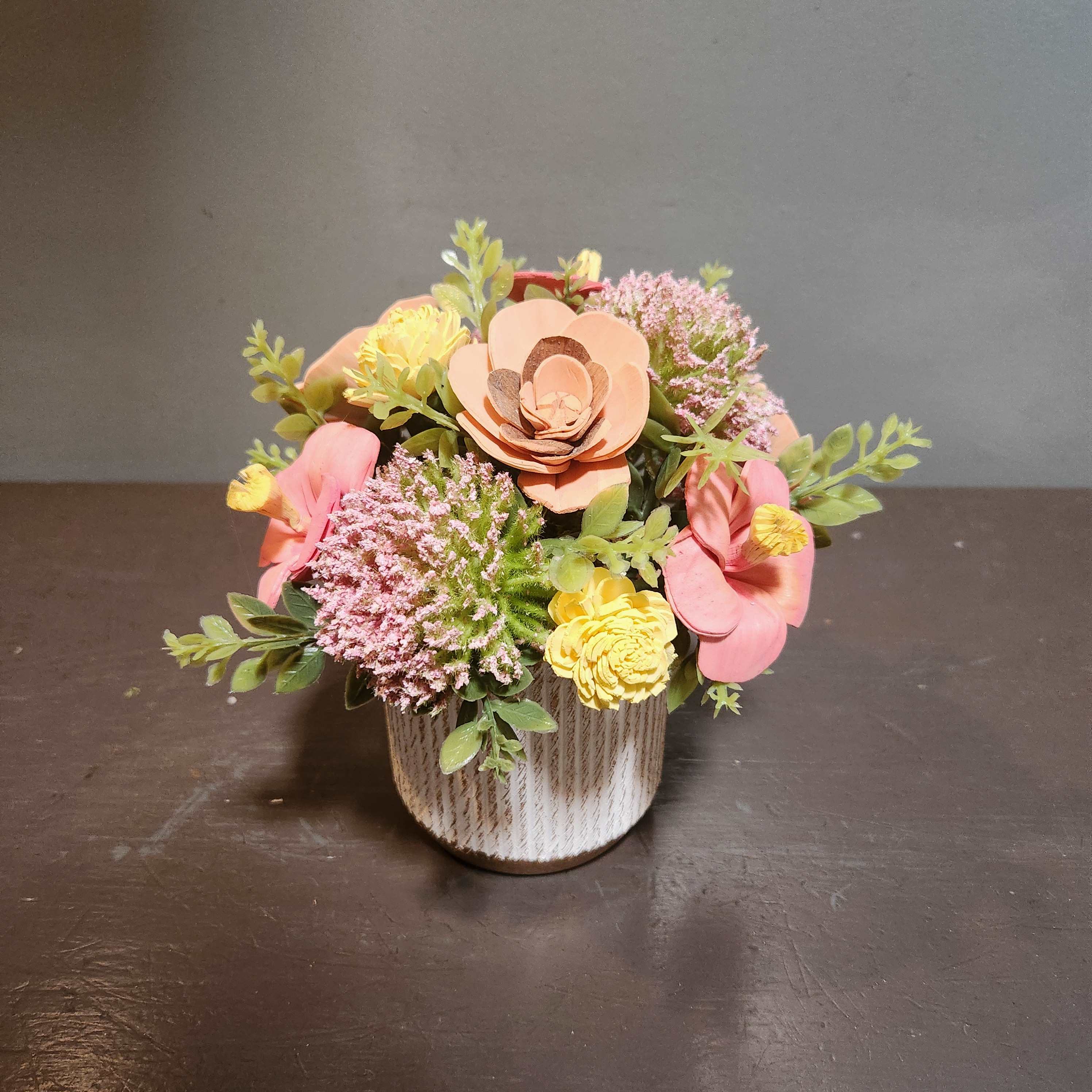 Small floral arrangement in a textured white pot with pink and yellow blooms