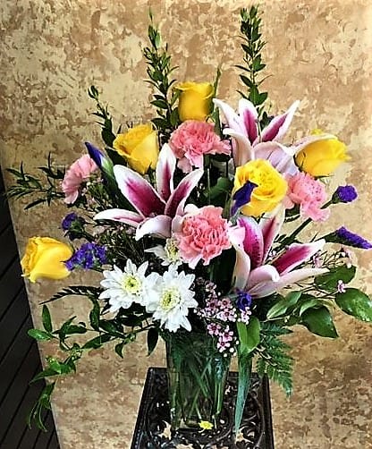 Mixed bouquet with pink lilies, yellow roses, and white daisies in a glass vase