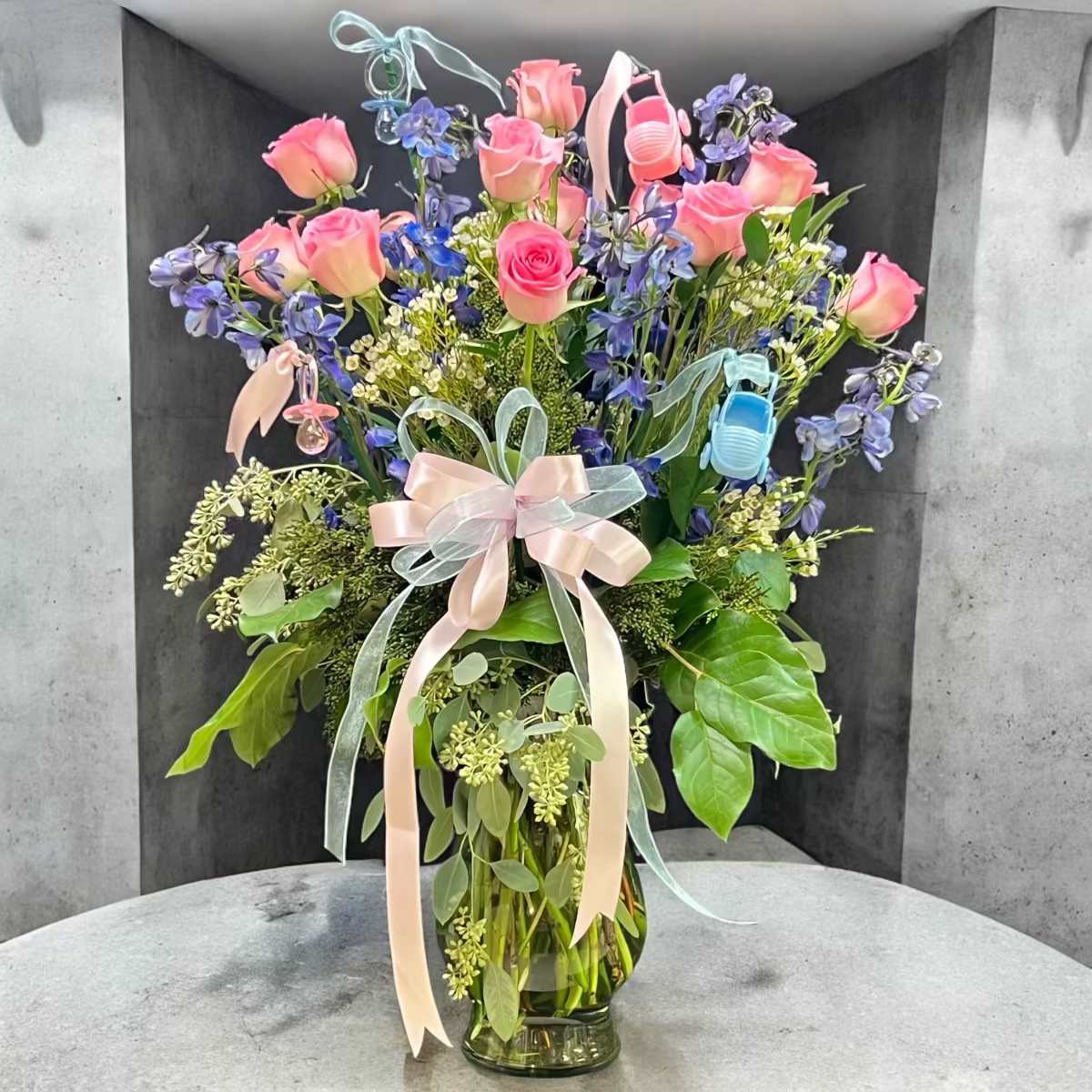 Pink roses and blue flowers in a glass vase with pastel ribbons