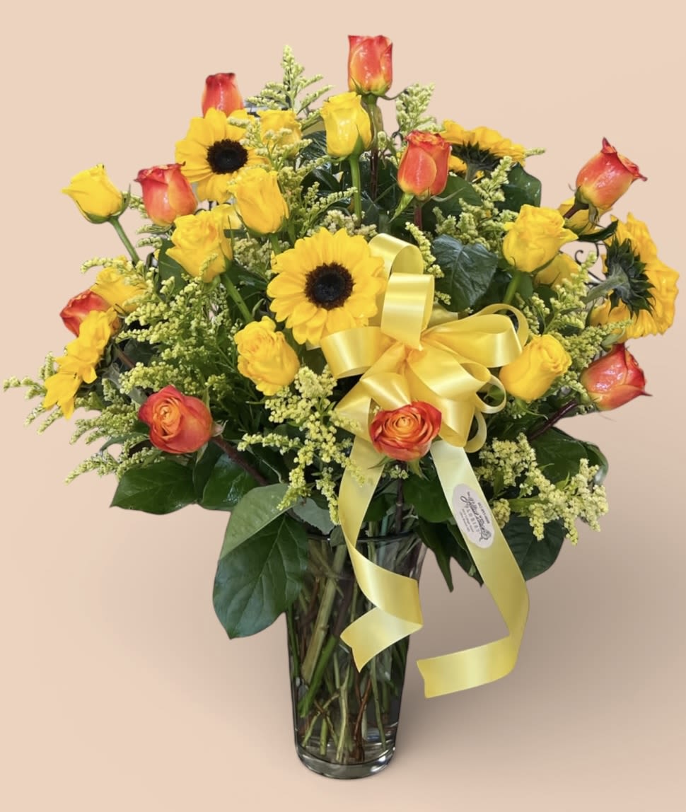 Sunflowers and orange-yellow roses in a clear glass vase with a yellow ribbon