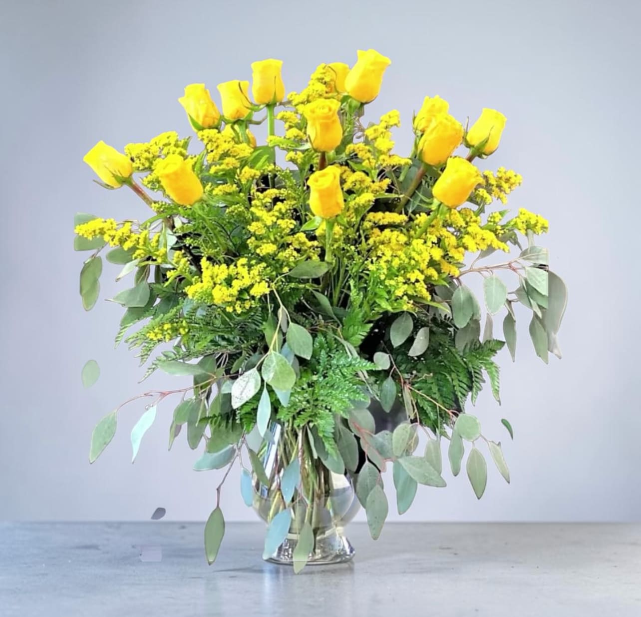 Two Dozen Yellow Roses - A beautiful design of Two Dozen Roses gathered in a clear glass vase with three types of beautiful greens and filler. 
