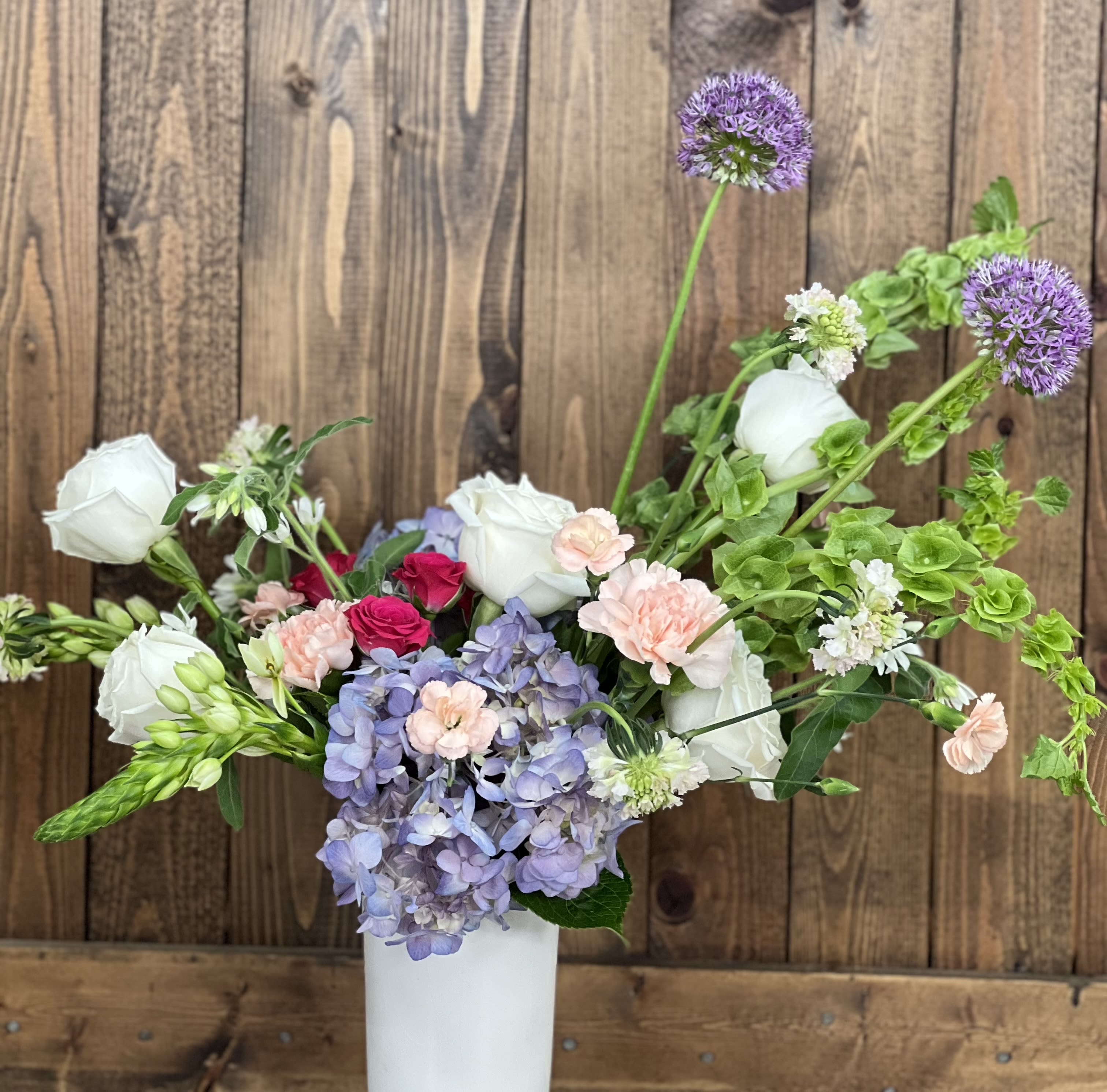 Mixed bouquet in a white vase with hydrangea, roses, and purple allium
