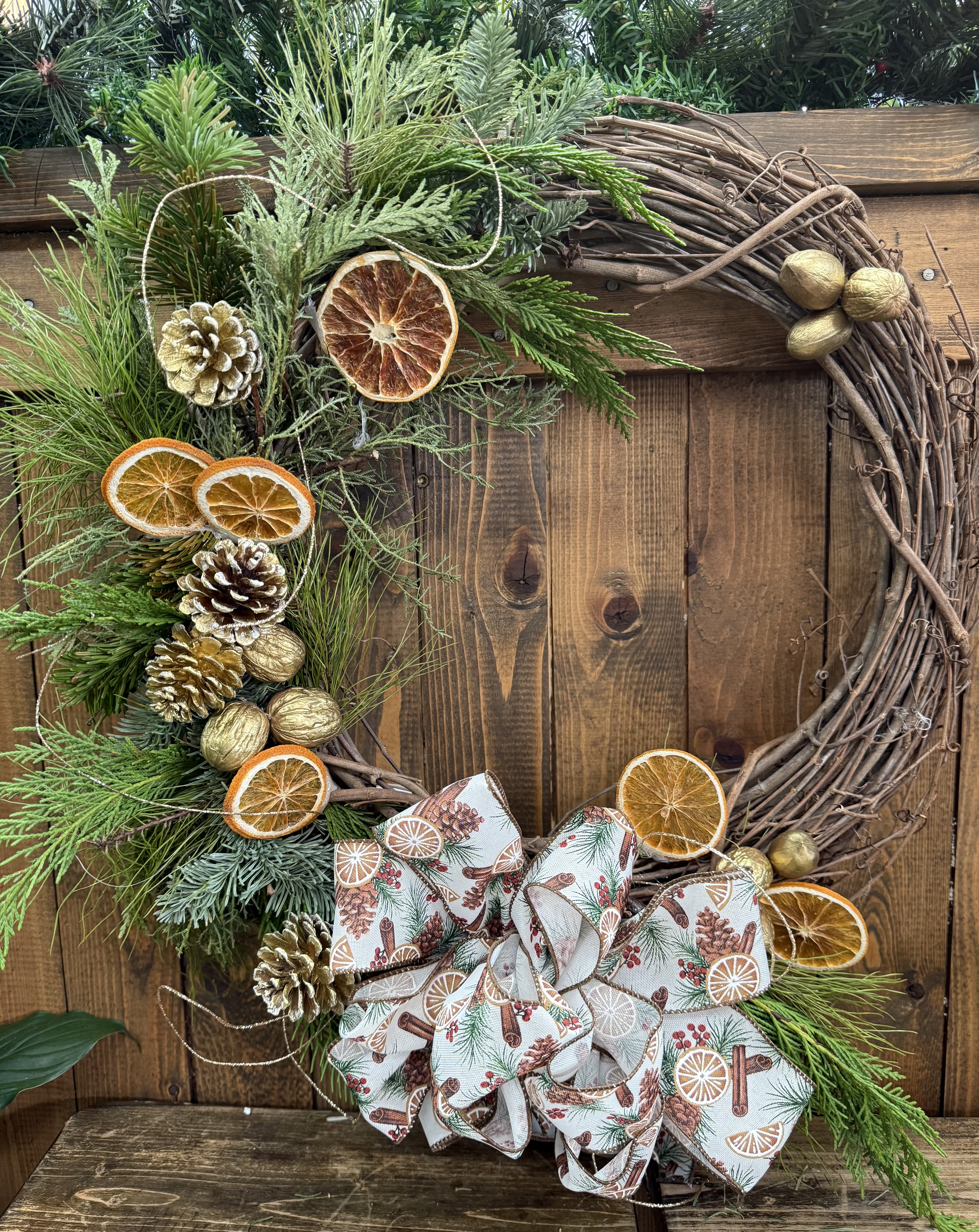 Holiday wreath with pine, dried citrus slices, pinecones, and a patterned bow