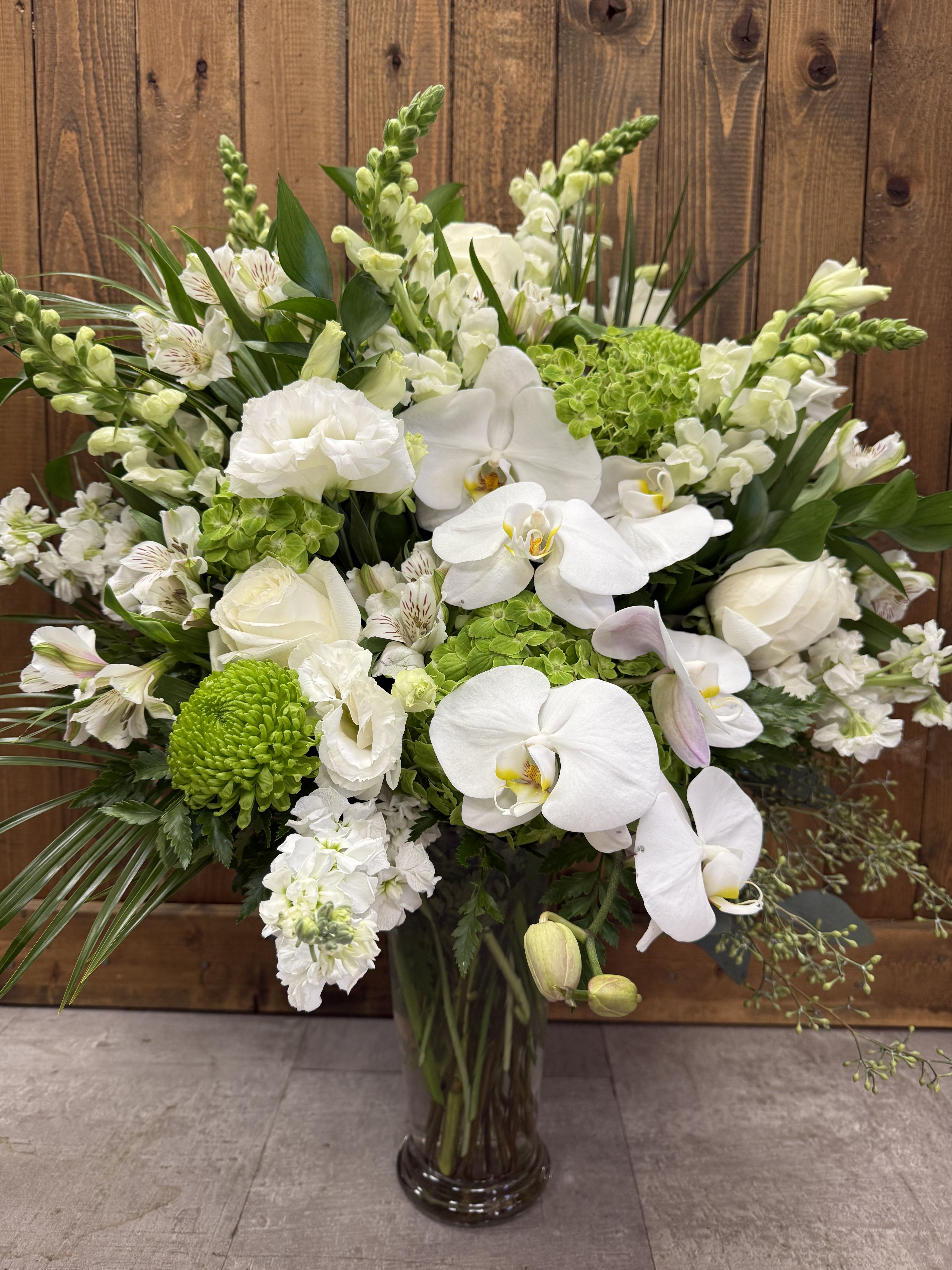 Tall white and green arrangement with orchids, roses, snapdragons and mums in a clear glass vase