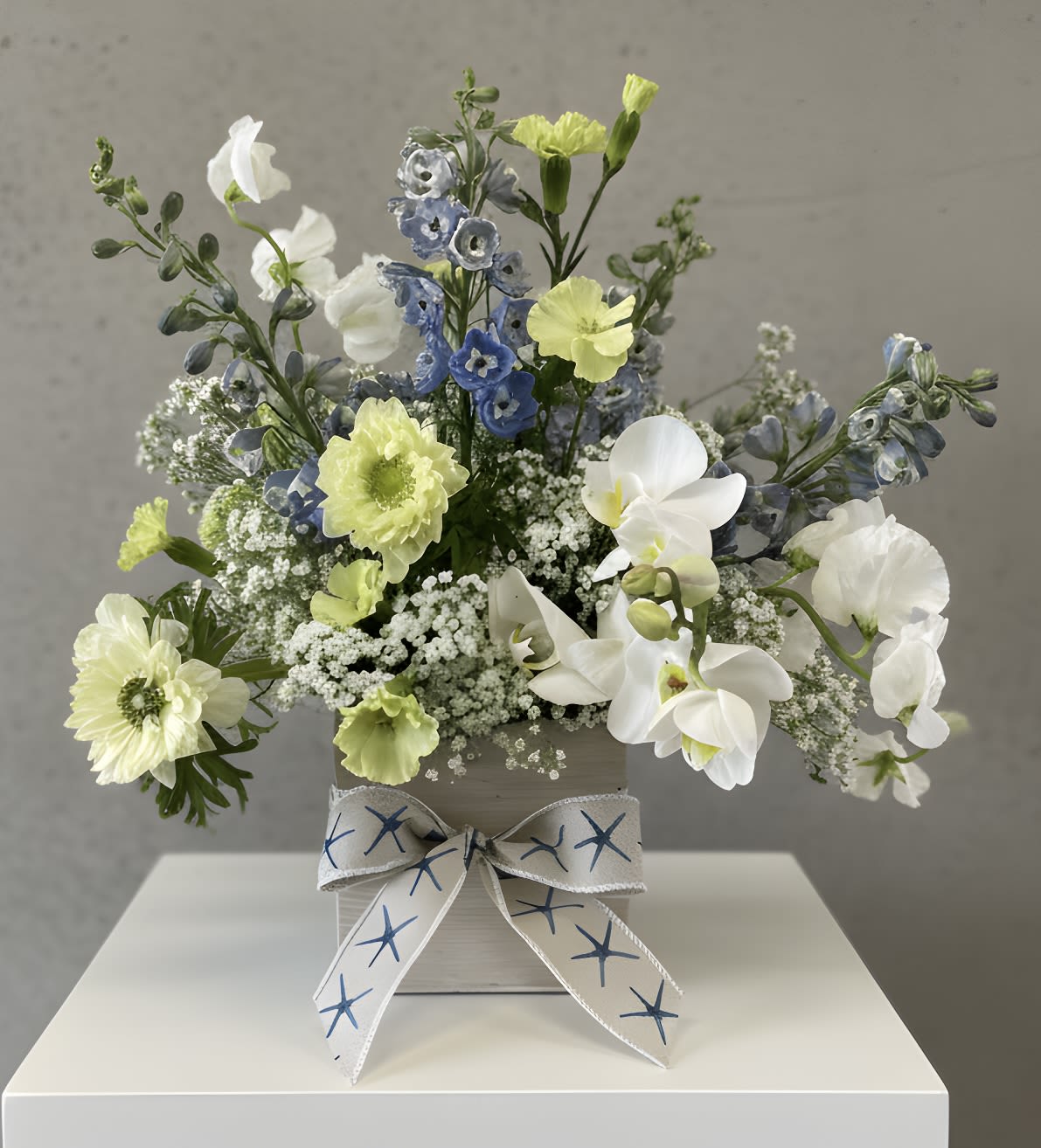 Seaside Whisper - A light, airy composition of soft blue delphinium, creamy white orchids and delicate sprays of baby’s breath makes this arrangement feel fresh like a seaside breeze captured in blooms. 
