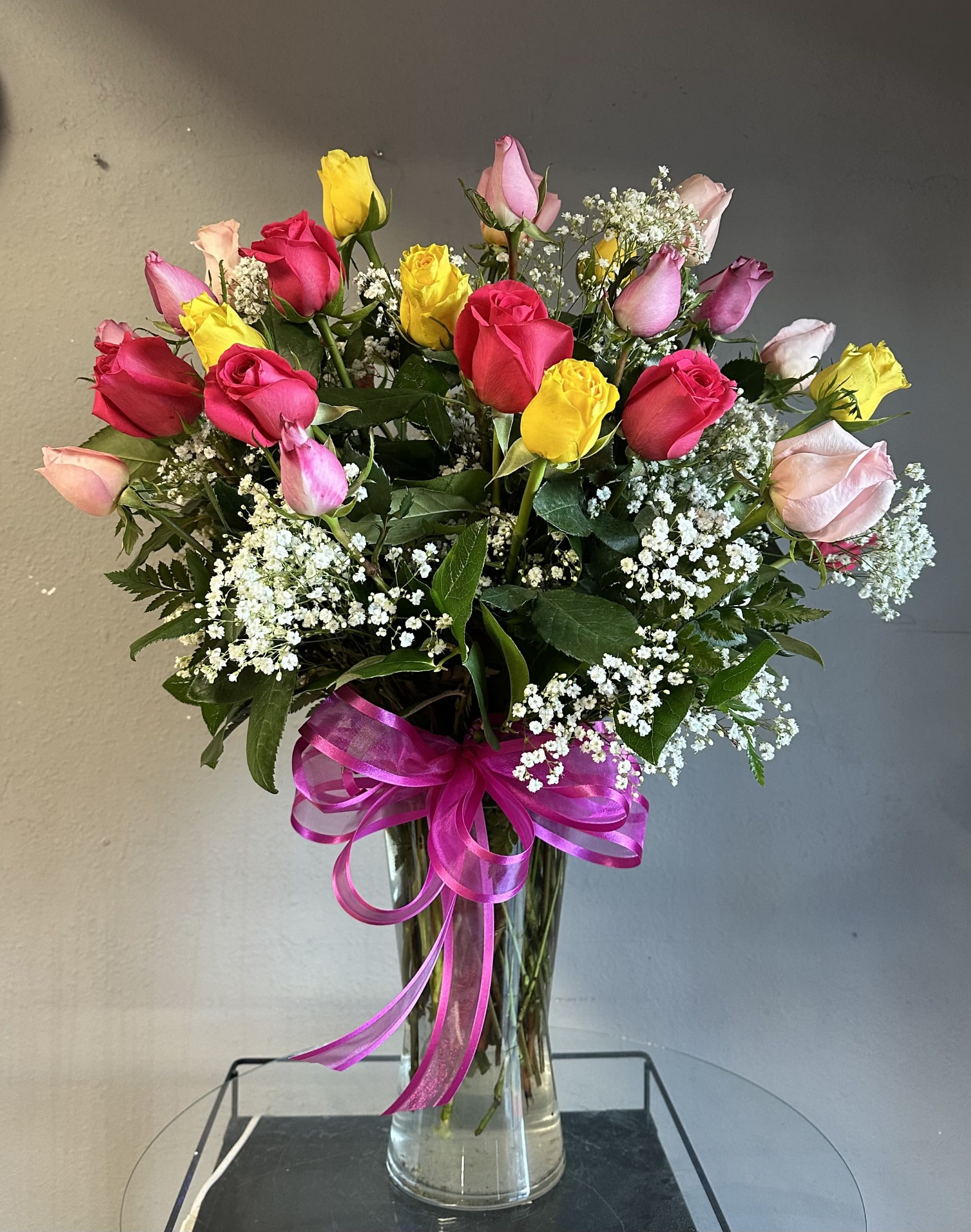 Bouquet of multicolored roses in a clear glass vase with a pink ribbon