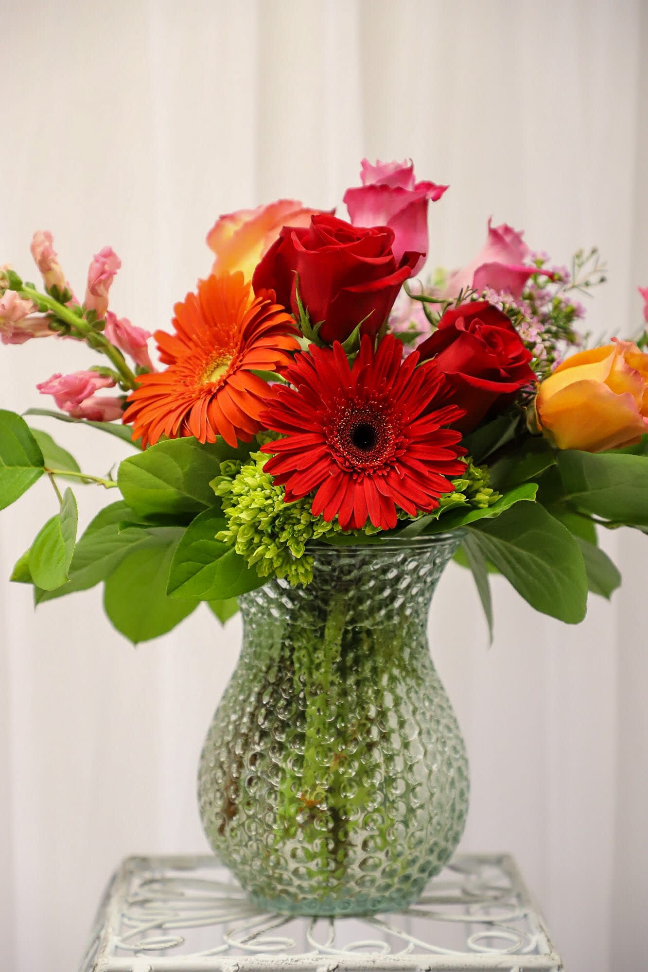 Mixed bouquet of red roses and gerbera daisies in a textured glass vase