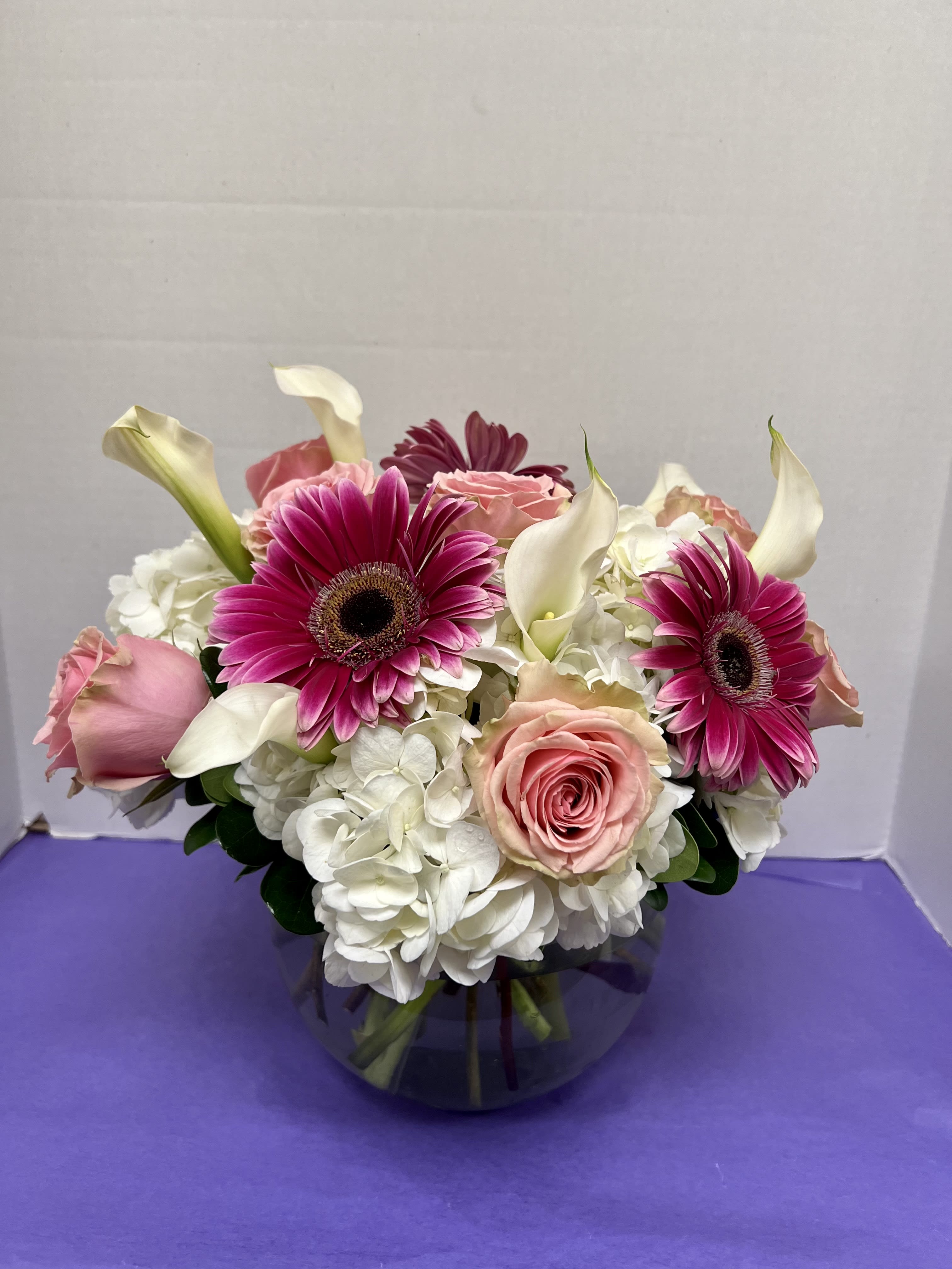 Pink gerberas, roses, white hydrangeas, and calla lilies in a glass vase