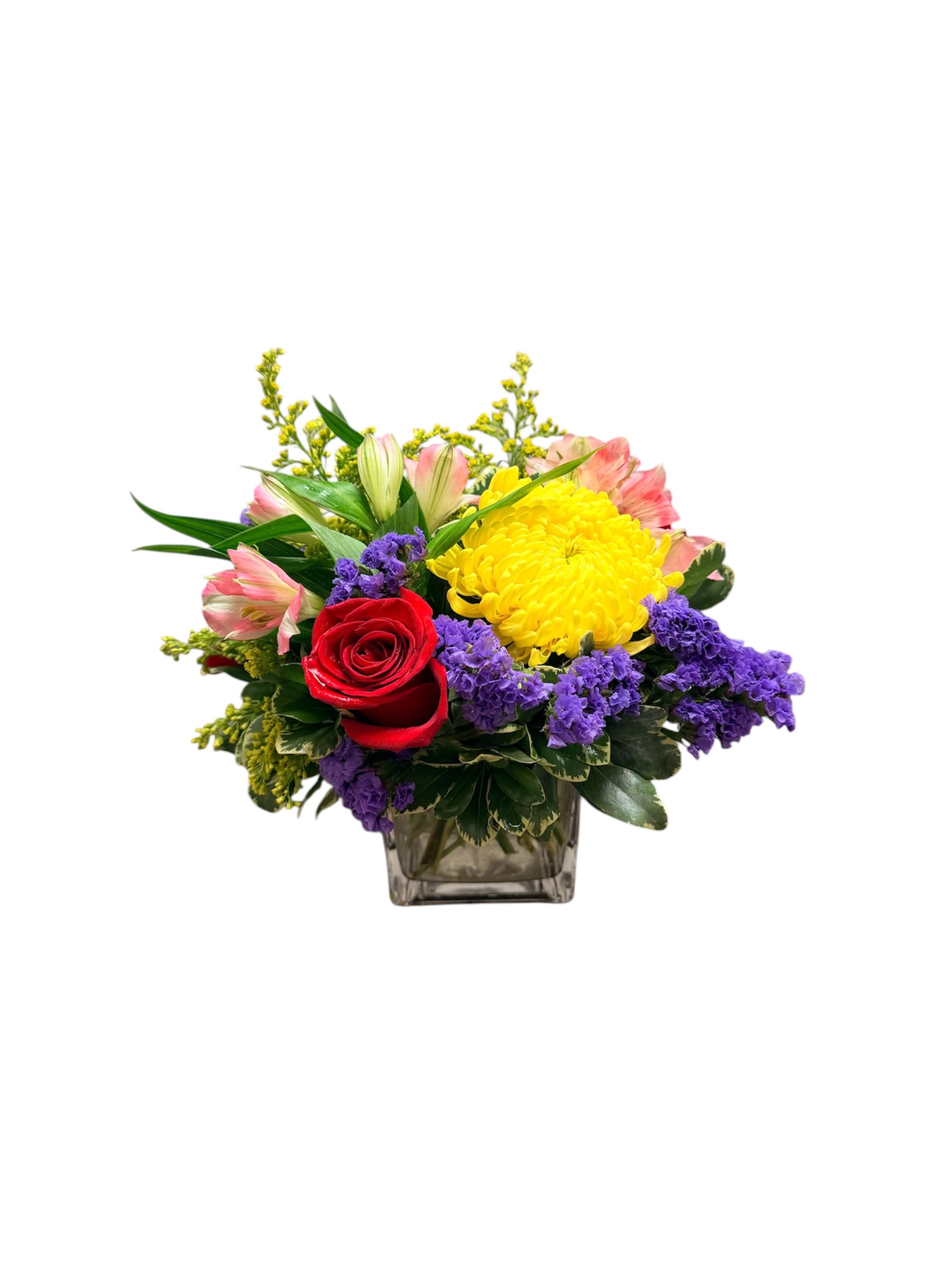 Short and Sweet - A compact burst of color centered on a red rose and a large yellow chrysanthemum makes this short, joyful flower arrangement perfect for a birthday, anniversary, or "just because" surprise. The mixed-color design-pink alstroemeria, purple filler blooms and cheerful chrysanthemums-creates a lively contrast that will make the person you're thinking of feel celebrated and noticed, whether you're sending congratulations, get-well wishes, or a New Baby greeting.  Tightly layered above a clear square glass vase, the arrangement reads bright and slightly formal: about a 4x4 cube composition that fits neatly on a bedside table, desk, or mantel. Textures range from the velvet of the rose to the airy alstroemeria petals and rounded chrysanthemum heads, offering visual depth in a small footprint. Ideal for graduations, Mother's Day, Thank You gestures, or to say "I'm sorry" with warmth-this petite design brings big emotion in a compact package.