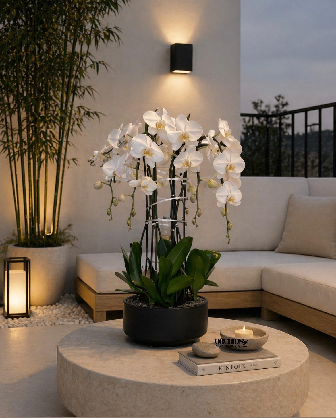 White orchids in a black pot on a round table with a candle and books