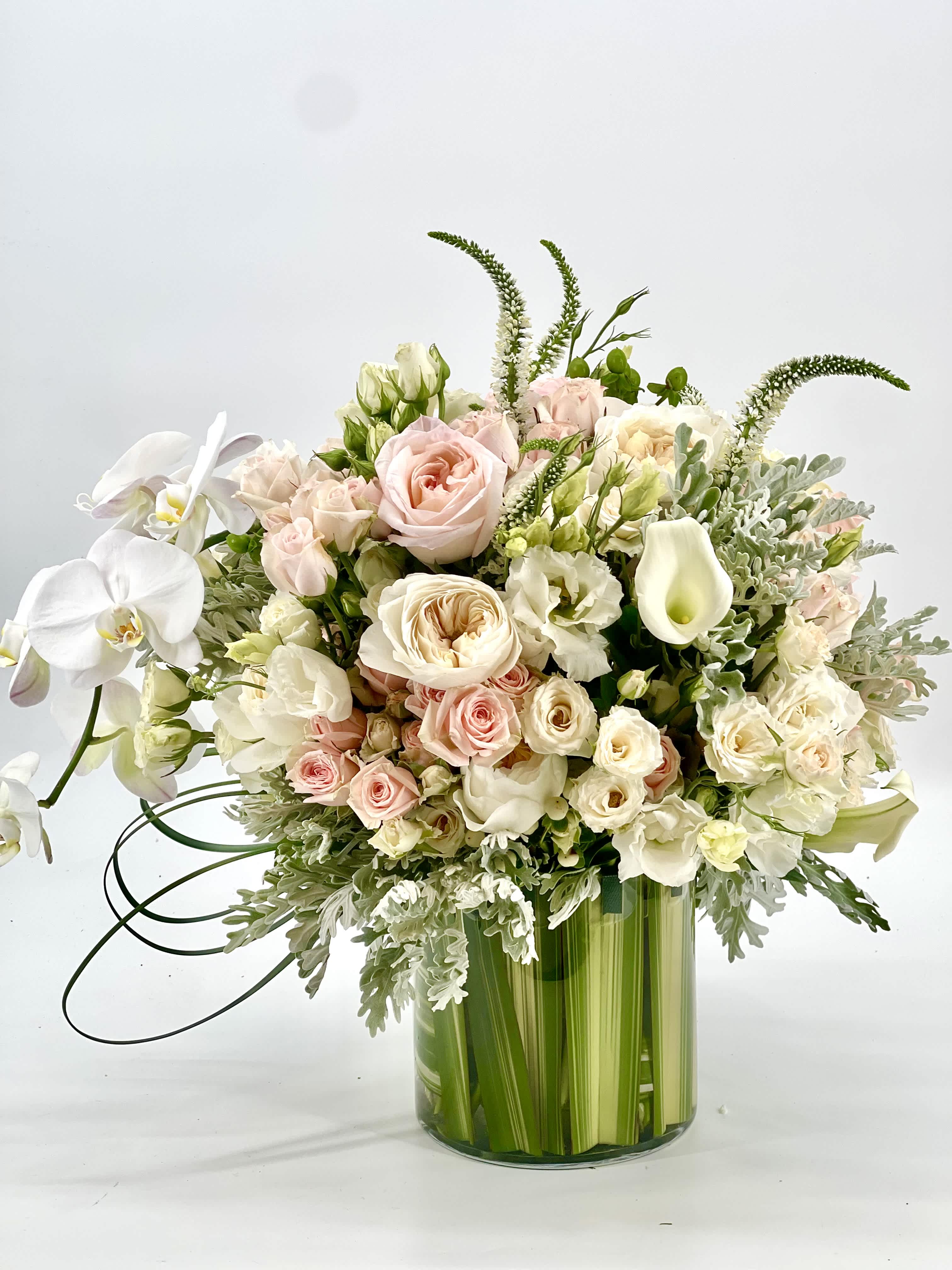 Pastel bouquet of roses, orchids, and calla lilies in a green glass vase