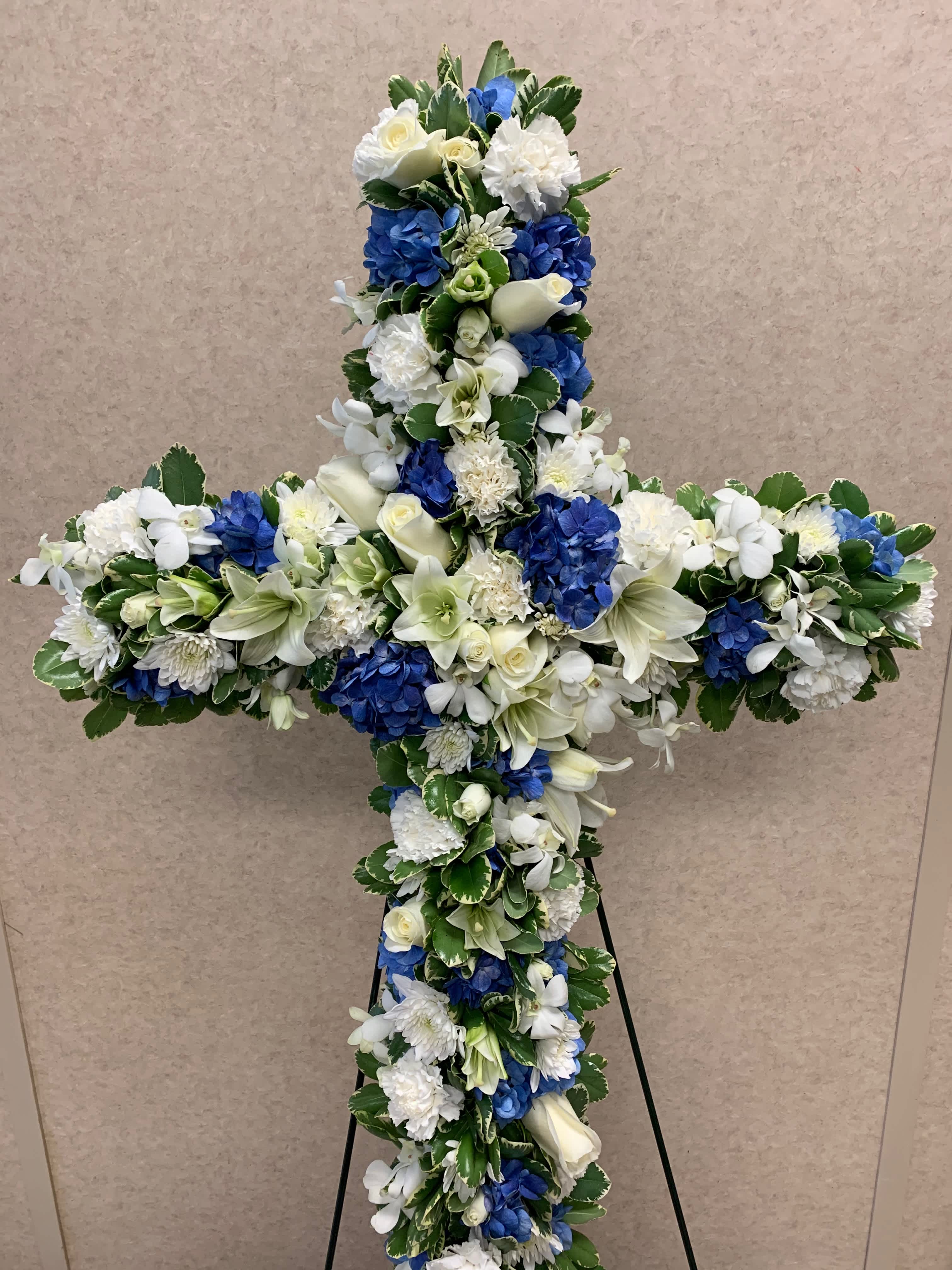 Cross-shaped floral tribute with white and blue flowers on a stand