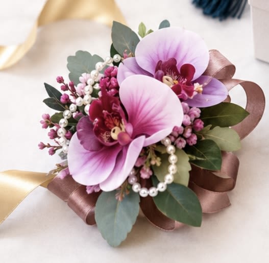 Orchid Pearl Wrist Corsage - Soft pink orchids paired with delicate pearl accents and lush greenery create an elegant wrist corsage perfect for prom, weddings, or formal celebrations. Finished with a satin ribbon for a timeless, romantic look.
