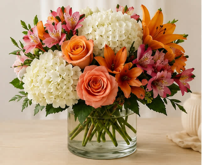 Bouquet of orange roses, lilies, pink alstroemeria, and white hydrangeas in a glass vase