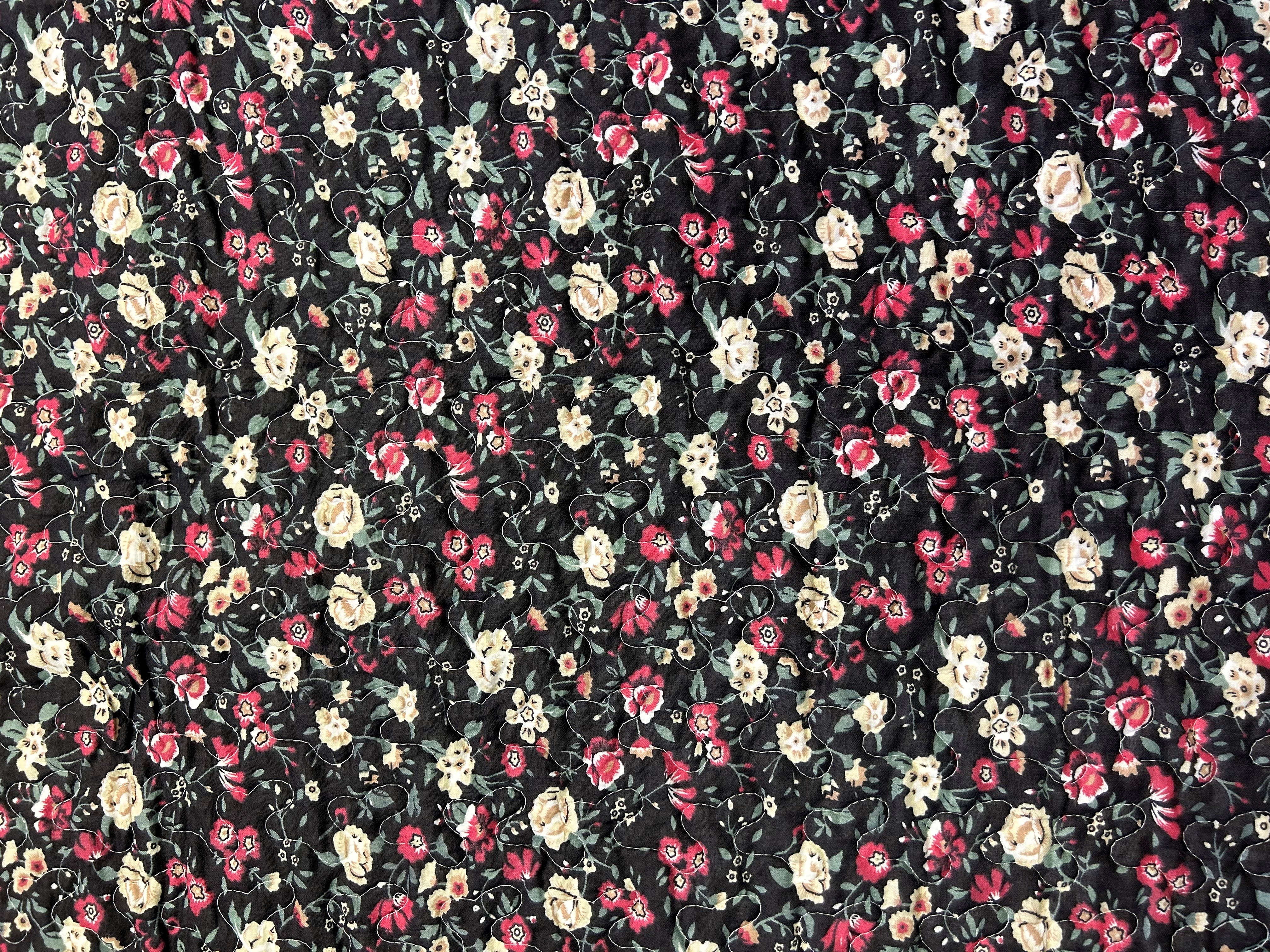 Black fabric with a dense floral print in pink, cream, and green