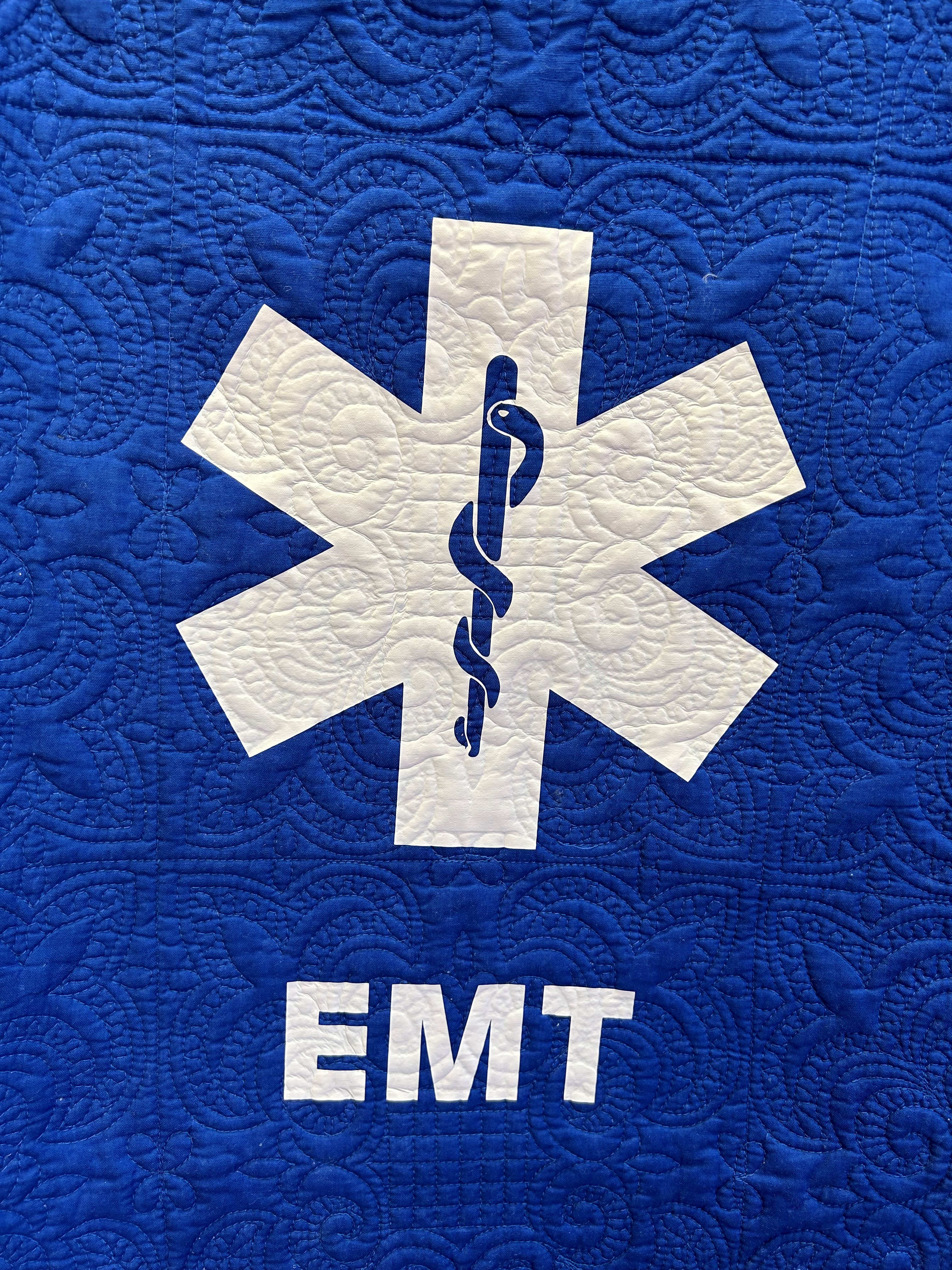 Blue quilted fabric with a white EMT medical symbol and text