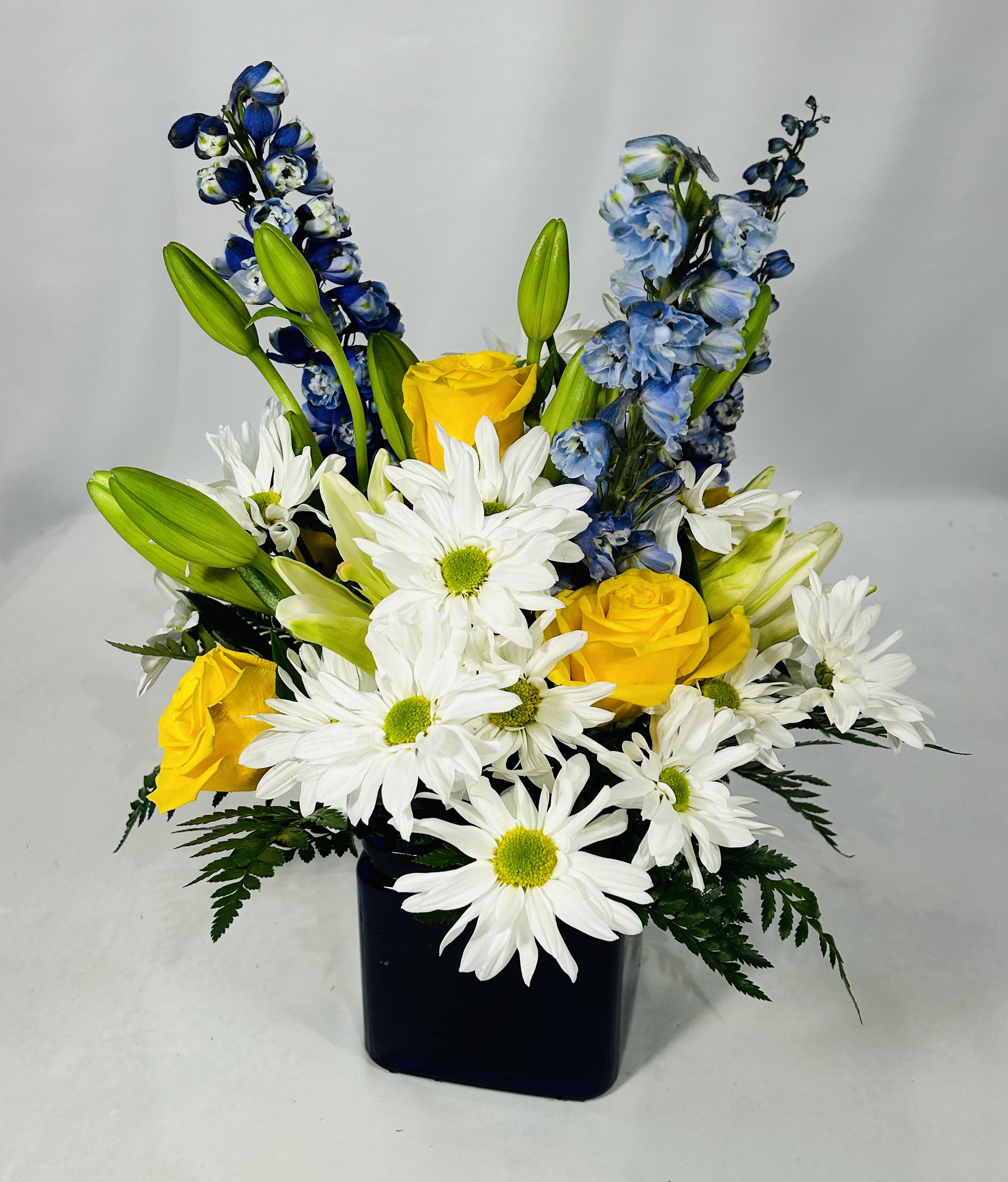Yellow roses and white daisies in a black vase with blue flowers