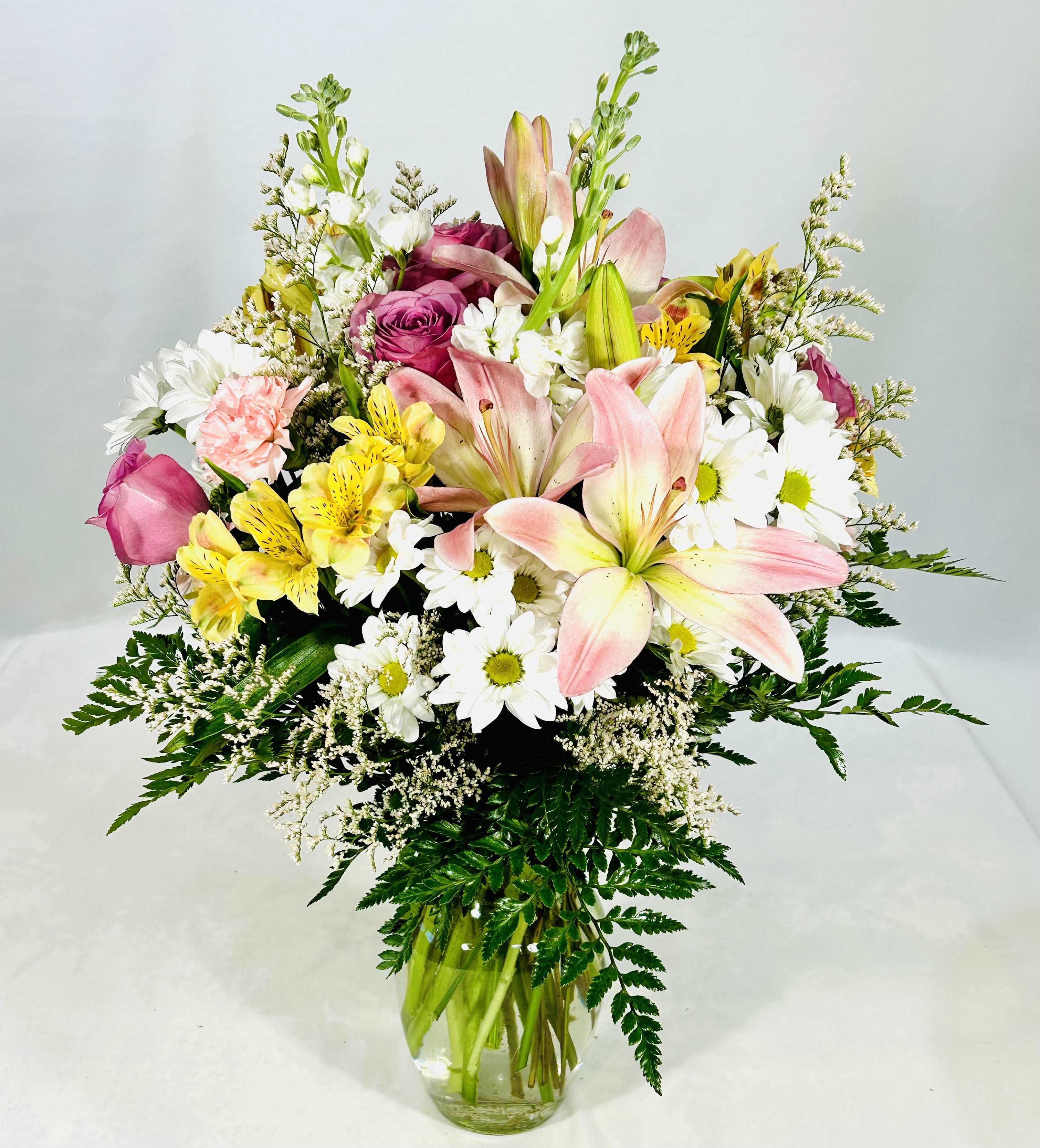 Spring Blossom  -  An eye-catching display of lavender roses and pink lilies is perfectly arranged to make a beautiful and lasting impression. Lavender roses, pink lilies, yellow alstromeria, white daisies and white stock arranged with greens.  18" H 15" W