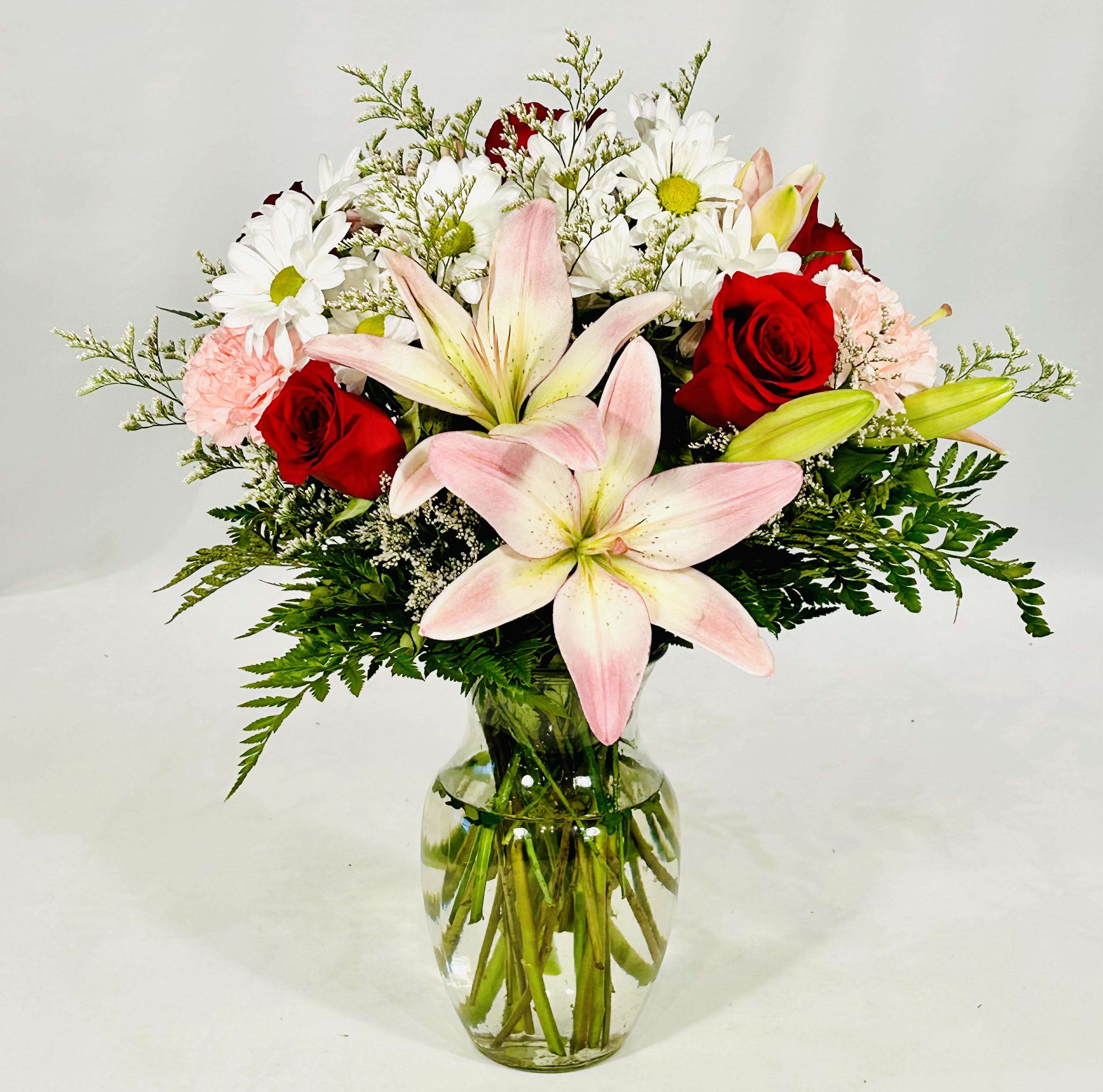 Bouquet of pink lilies, red roses, and white daisies in a glass vase
