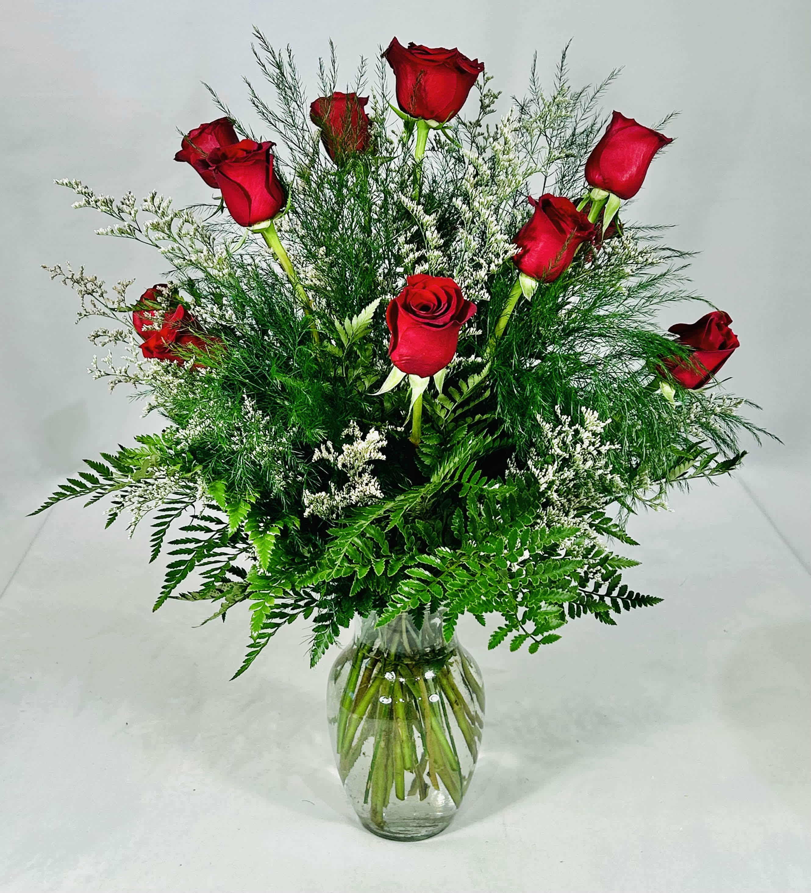 Red roses arranged in a clear glass vase with airy greenery