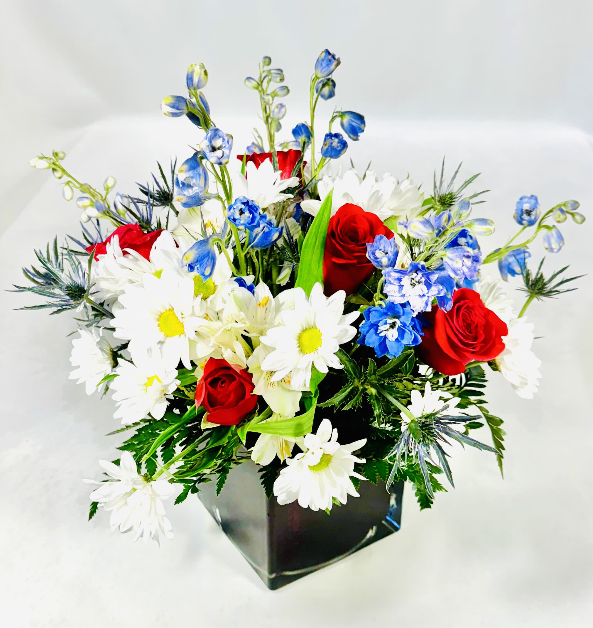 Red roses, white daisies, and blue flowers in a black vase