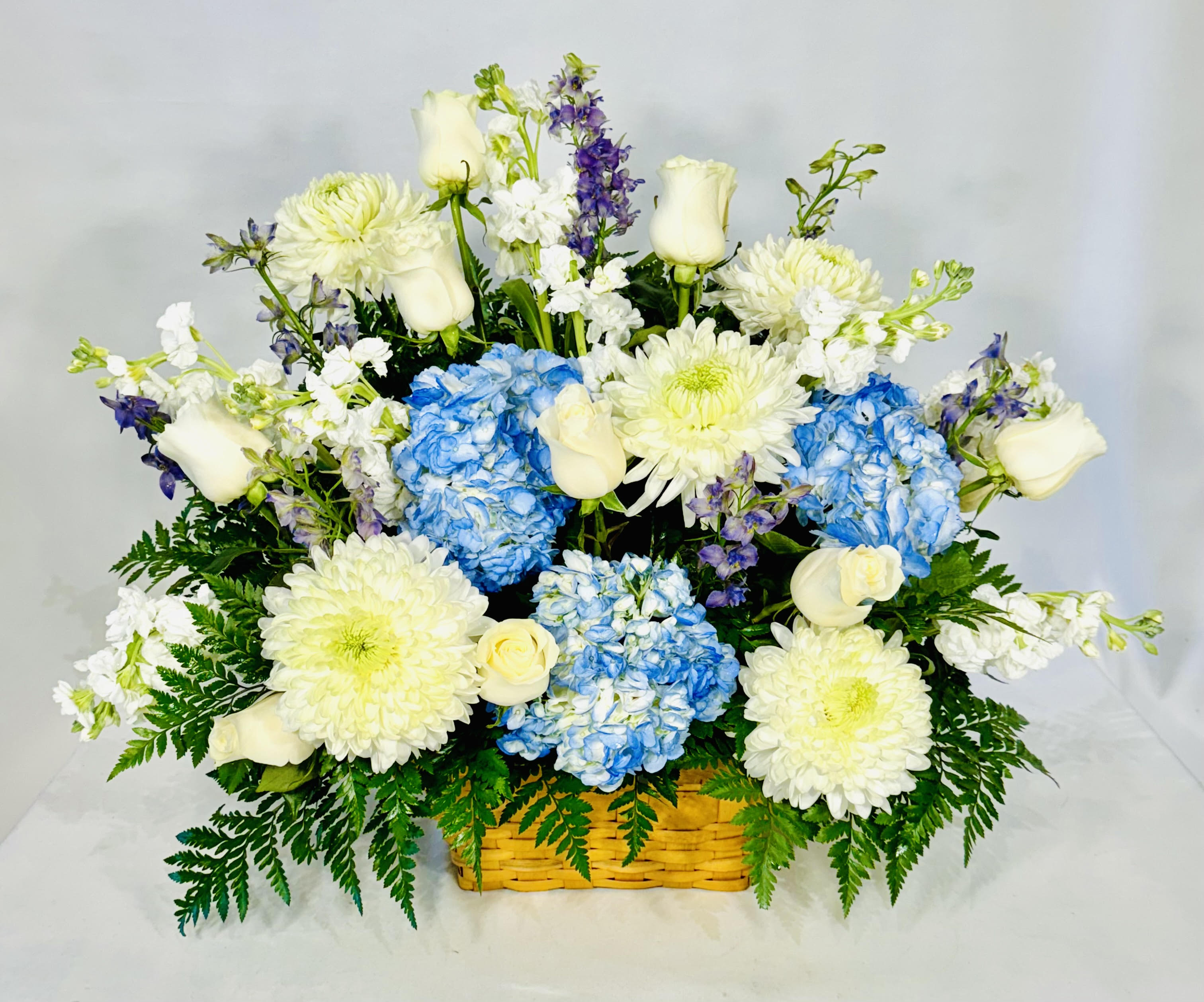 Basket arrangement of white roses, blue hydrangeas, and white chrysanthemums