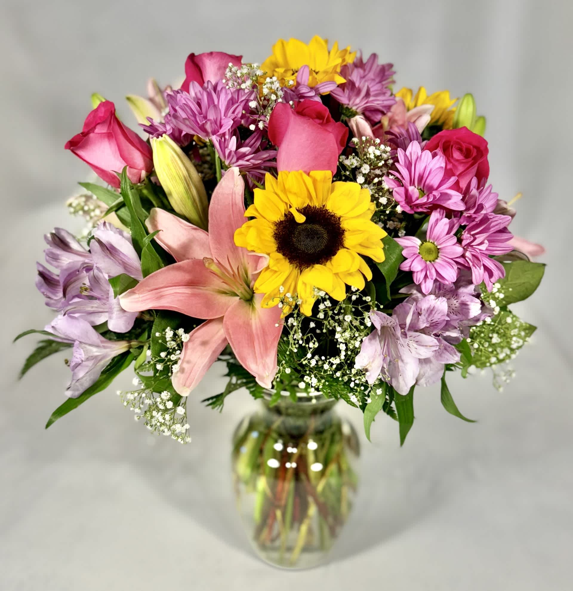 Summer Sun  - This Summer Sun arrangement is perfect for any occasion! It will definitely brighten up anyone's day. This stunning arrangement includes sunflowers, hot pink roses, pink lilies, lavender daisies, pink alstroemeria, purple carnations and Limonium.  16" H