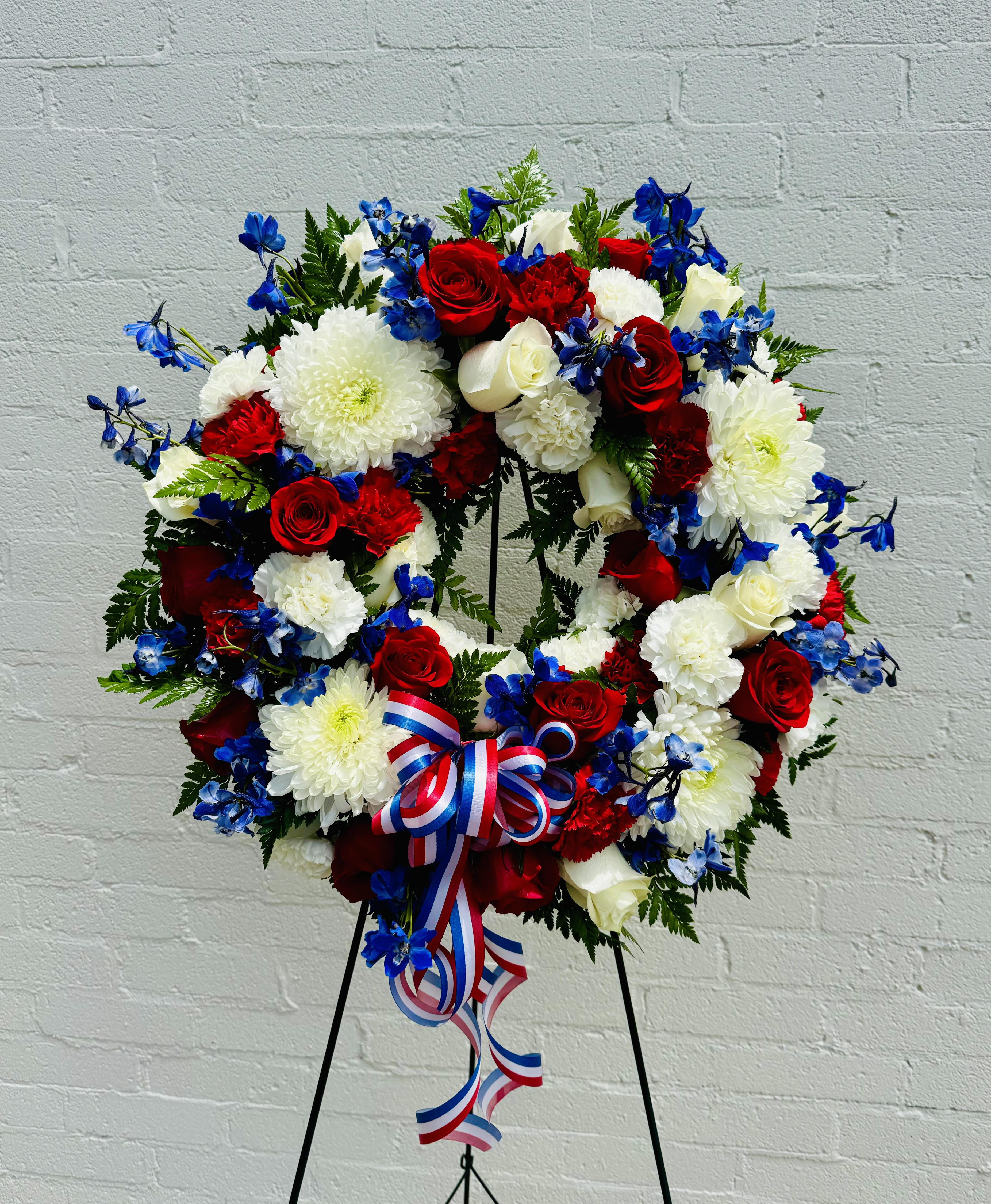 Red, white, and blue floral wreath on a stand with ribbon
