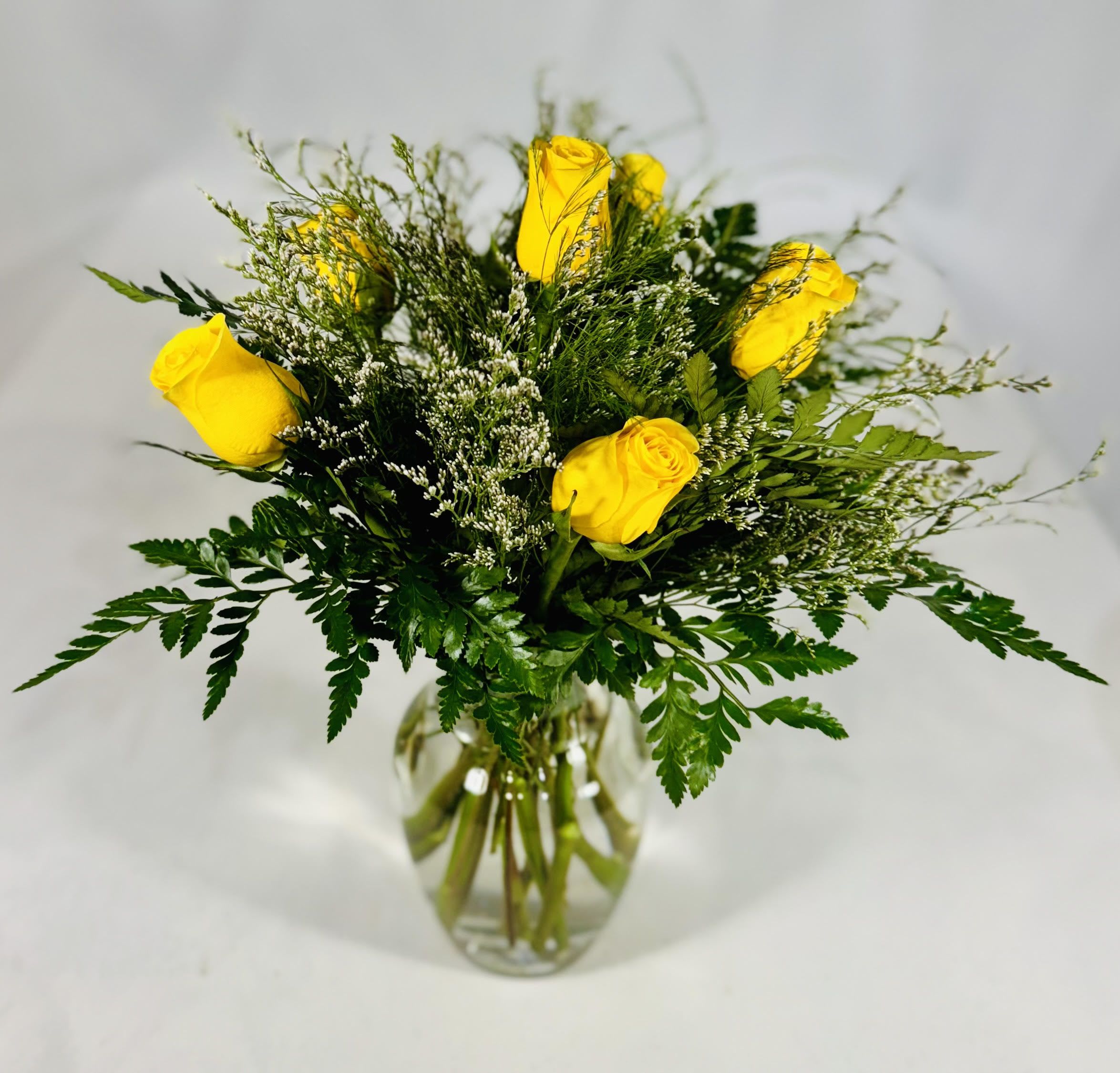 Yellow roses in a clear glass vase with airy greenery