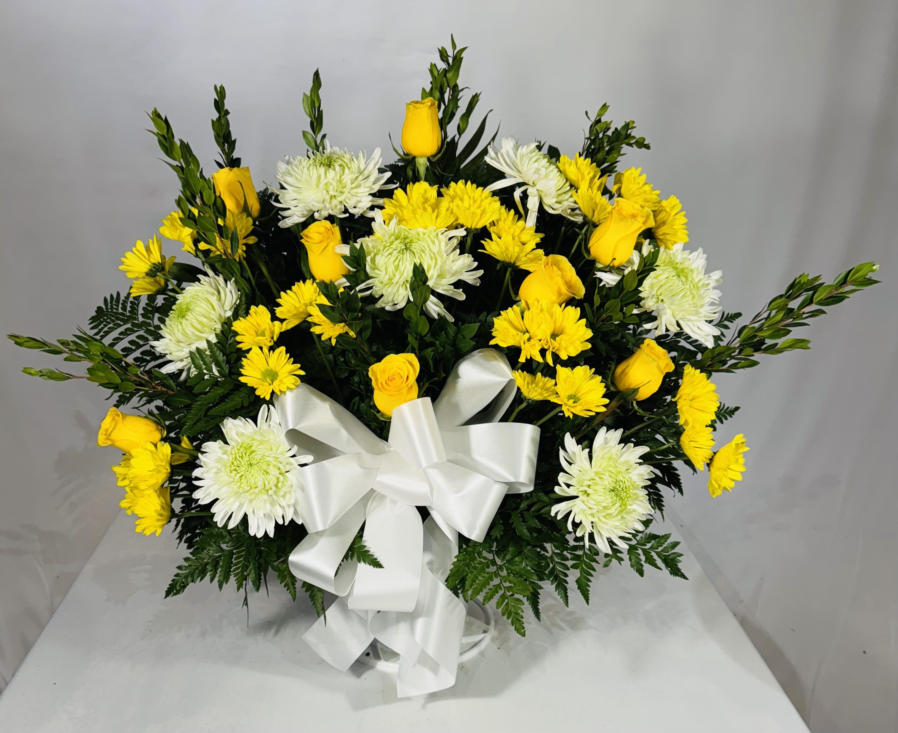Yellow roses and white chrysanthemums arranged with a white ribbon bow