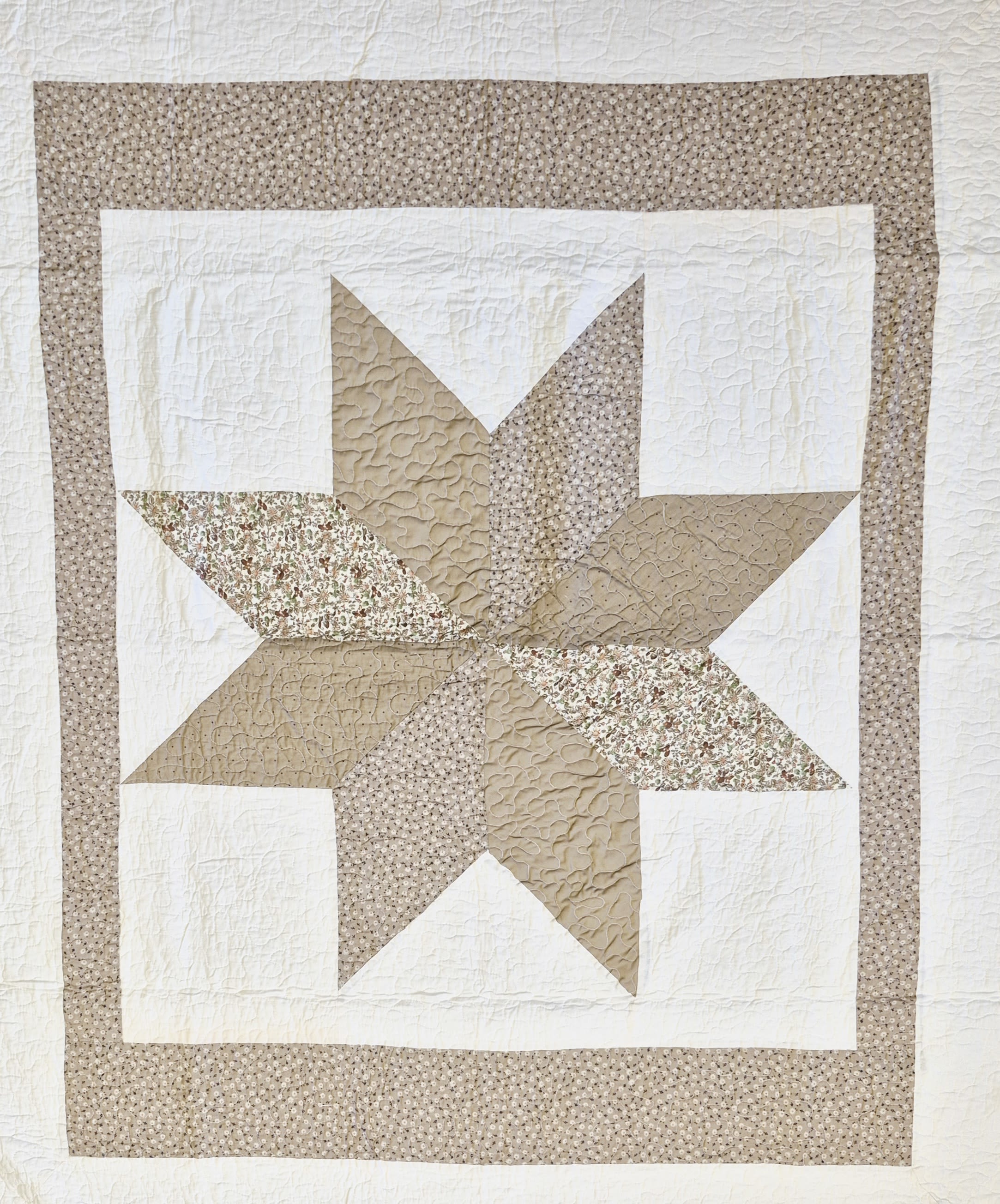 Khaki Star Quilted Throw  - A handcrafted khaki star quilt brings quiet comfort and timeless style to anniversary, housewarming, or sympathy gifts-perfect for saying "thinking of you" with warmth. The 50 x 60 throw features a large eight-point star pieced from beige and taupe prints, including small floral motifs, set against a soft white ground; its neutral palette makes it equally right for birthdays, retirement celebrations, get-well wishes, or a simple "just because" surprise for the person you're thinking of.  Subtle quilting stitches add tactile texture and a homemade feel that will make the recipient feel seen and soothed. The throw pairs beautifully with the metal easel stand (available as an add-on for presentation) when you want an elegant display for a funeral, memorial, or gallery-style gift reveal. 