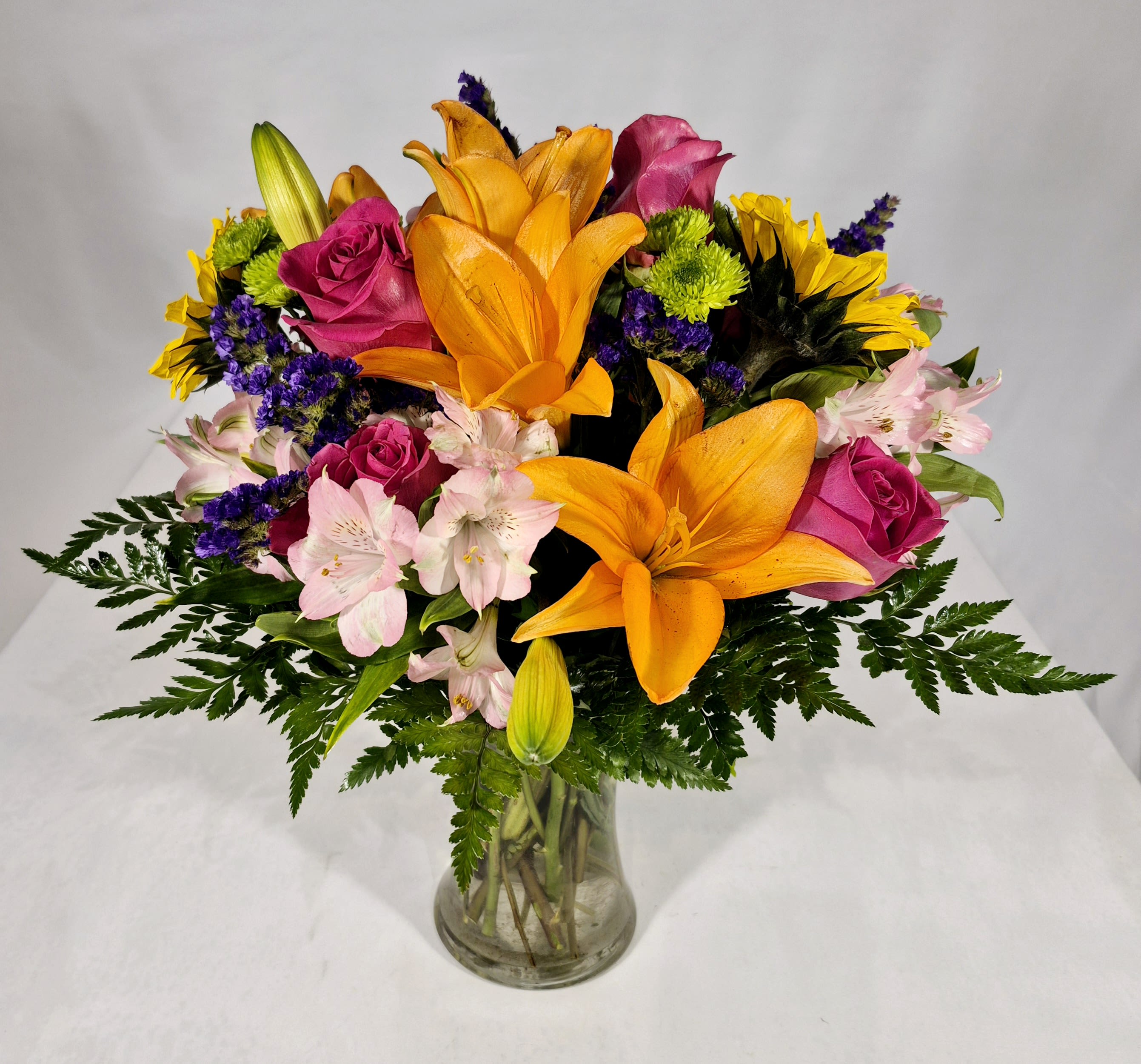 Vibrant Floral Meadow - Putting a smile on someone's face to start their day starts with a beautiful gift. Our delightfully vibrant floral bouquet is filled with a combination of blooms in cheerful pops of orange, pink, purple and yellow, with plenty of lush greenery mixed in.  16" H x 12" W