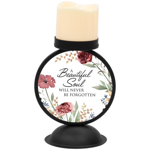 "Beautiful Soul" Lighted Candle Holder - Softly lit and quietly comforting, this lighted candle holder designed to honor a loved one. As a memorial gift for a funeral or to bring solace at home, the piece reads "A Beautiful Soul Will Never Be Forgotten" surrounded by illustrated blooms in pink, red, white and muted earthy greens-an arrangement of color that feels both gentle and dignified for remembrance.  The decorative LED pillar candle sits on a sturdy black round metal stand with a wide base and a printed round plaque at the front featuring floral artwork and the memorial sentiment. The warm ivory candle top and included LED light create a steady, flameless glow; the holder is powder-coated for weather resistance and finished in high-quality metal. Practical details: the holder measures approximately 5.5" wide x 10" high x 4.5" deep, includes an ON/OFF switch and comes with 3 AAA batteries.  Give this keepsake to someone who needs a lasting expression of sympathy-a private bedside tribute, a mantelpiece remembrance, or a comforting accent at a memorial service. It arrives ready to display and provides a gentle, maintenance-free light that helps keep memories present long after the flowers fade.
