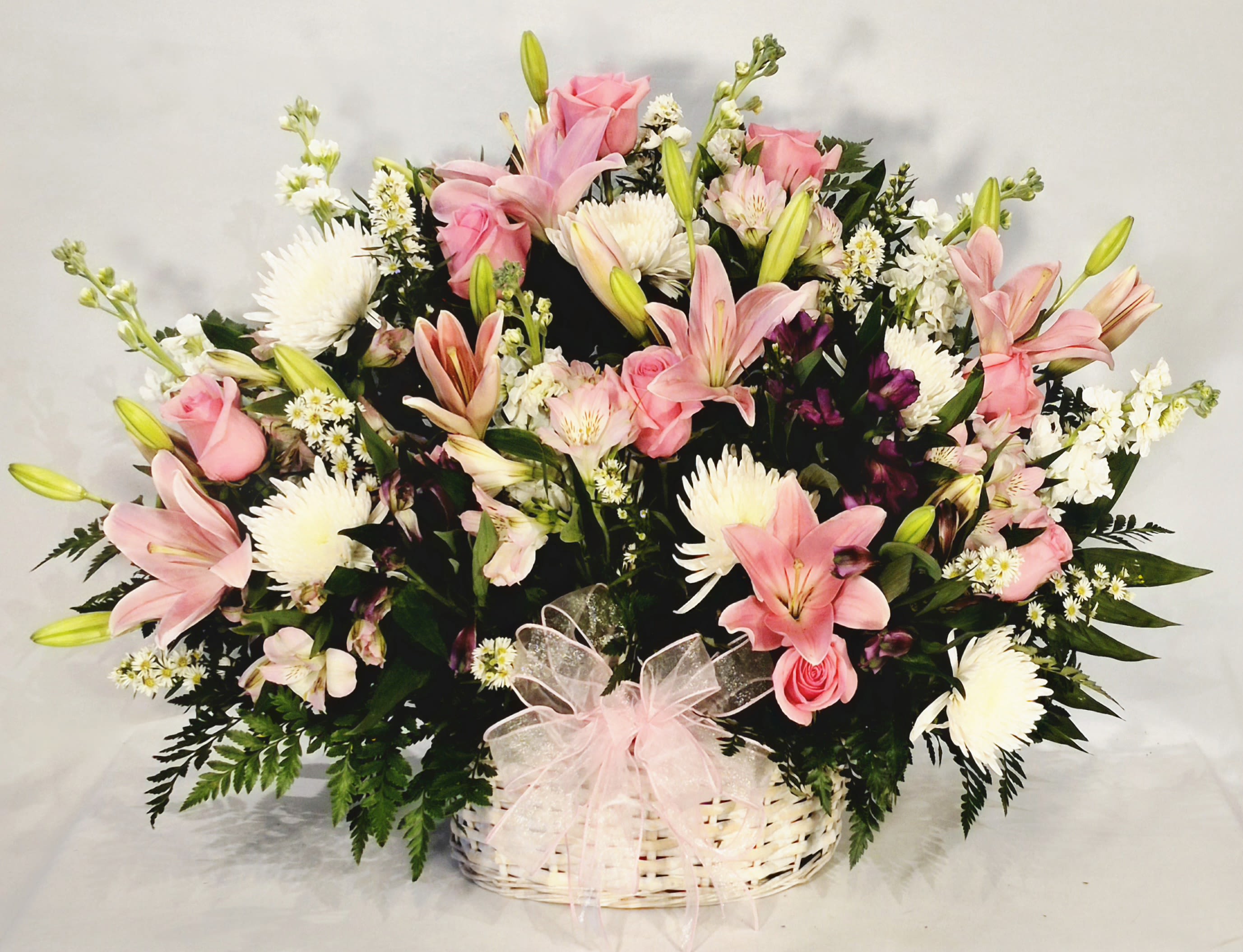 Pink lilies and roses in a white basket with a pink bow