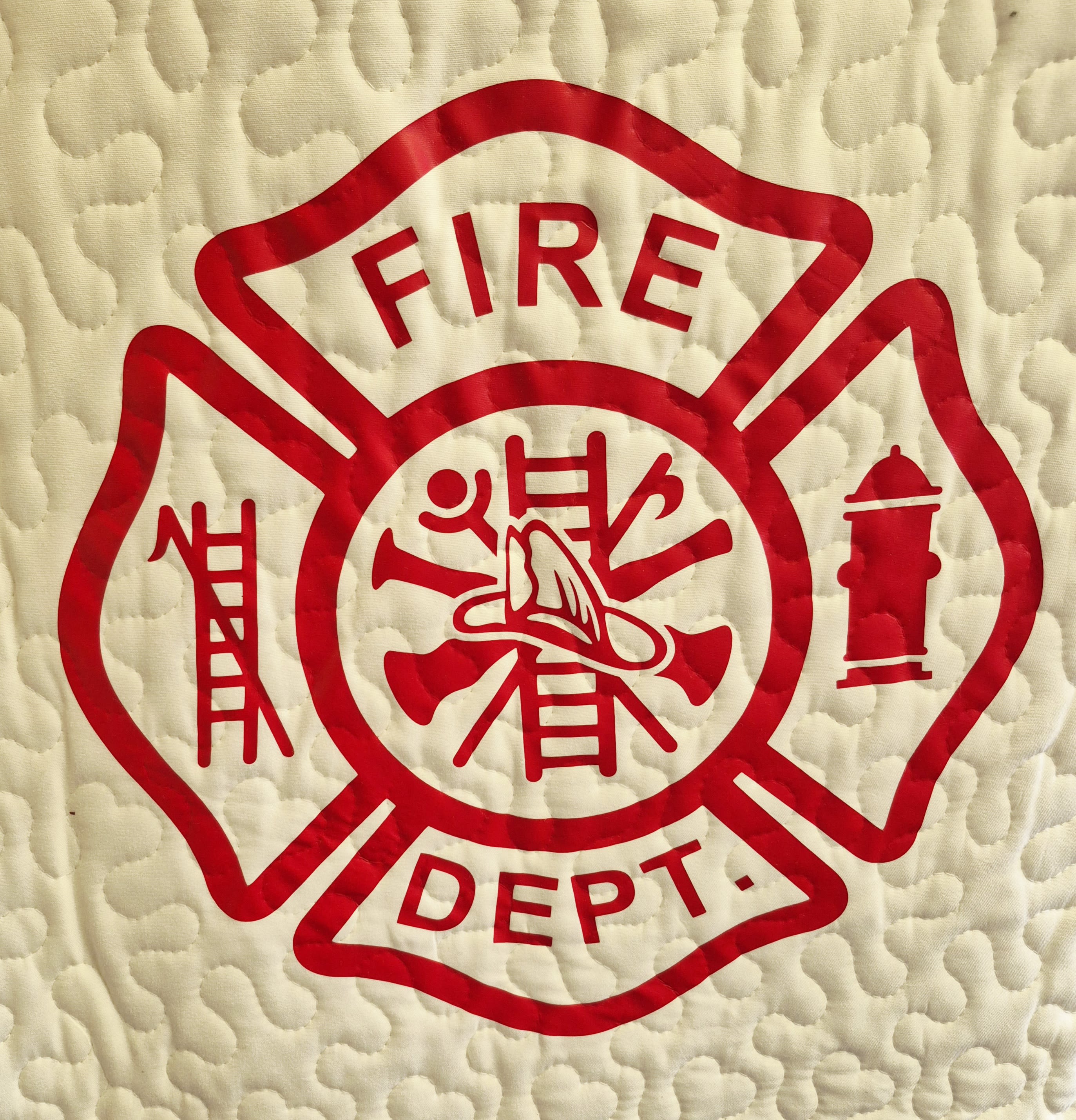Firefighter Quilt  - A bold red-and-white firefighter tribute designed to honor service and memory-perfect as a sympathy or funeral floral accompaniment, a retirement gift, or a meaningful birthday present for the person who served. The quilt's patriotic palette of red and white reads clearly from a distance and will make the recipient or their family feel seen and respected during a solemn moment or celebration.  The quilt measures 50 x 60 inches, finished with scalloped edging and vivid red lettering on a white field for a clean, traditional look. The listing pairs the quilt with an optional wire easel stand. Select the Deluxe option to add the easel to your order for a polished presentation; the easel is available for an additional charge.  Appropriate year-round for memorials, retirements, Father's Day tributes, or a firefighter's birthday, this keepsake sends a clear message of honor and appreciation to the family or the person you're remembering. 