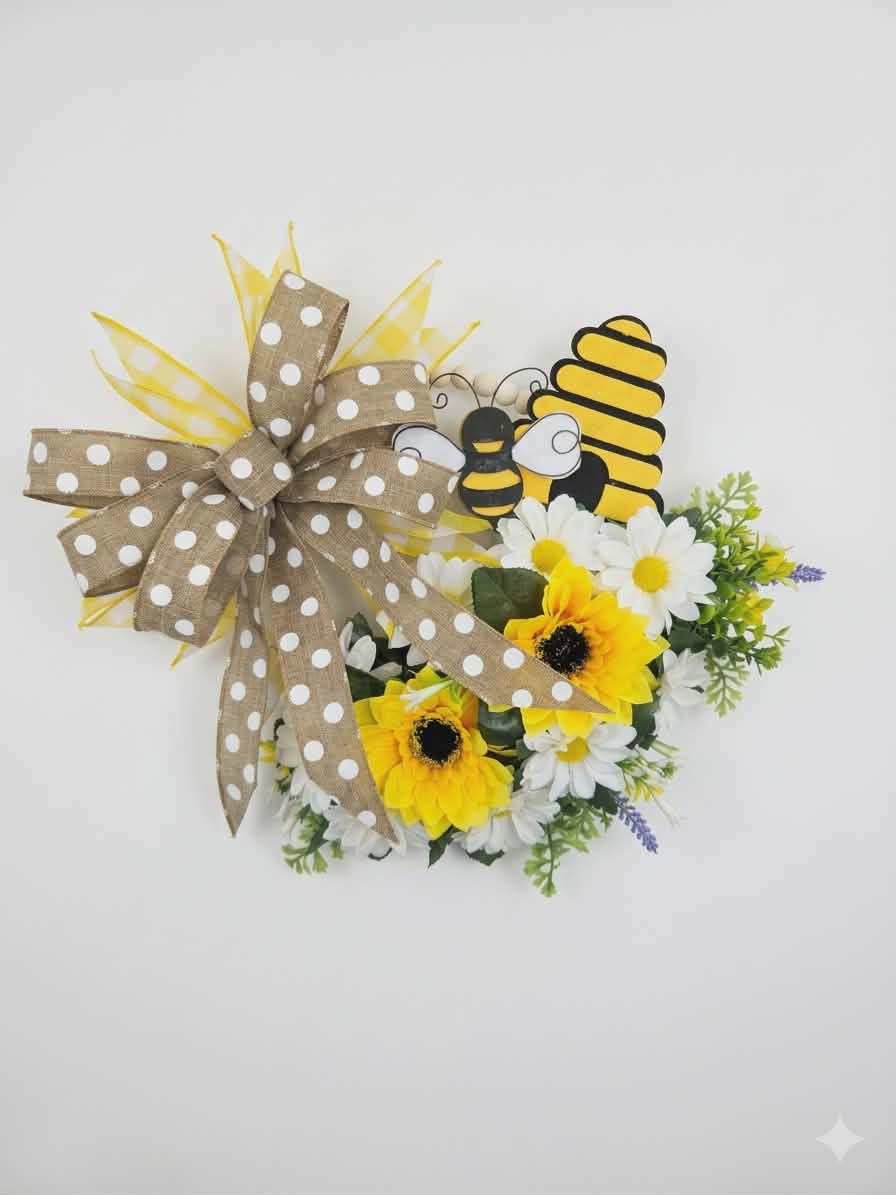 Welcome to Our Hive Wreath  - Bright yellow sunflowers and crisp white daisies cluster along the lower half of this wreath-style flower arrangement to create a cheerful, springlike welcome - perfect as a front-door decoration or a sunny housewarming gift. The playful garden theme, complete with bee decorations and yellow accents, makes this wreath an ideal everyday display for spring, summer, or anytime you want to lift someone's spirits.  Natural textures and rustic charm come from a burlap polka-dot ribbon bow tied to the wreath form, while mixed greenery and varied bloom sizes add depth and movement. Sized at approximately 20" tall and 16" wide, this compact wreath fits most doors and entryways and arrives ready to hang as a bright, homespun accent that will make the person you're thinking of feel warmly welcomed.