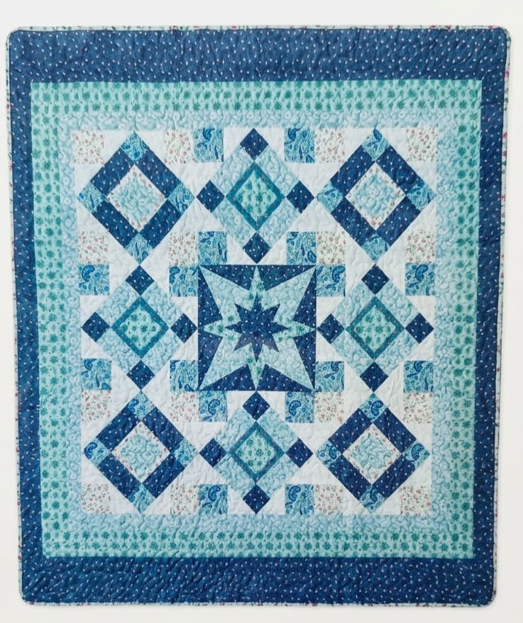 Turquoise &amp; Shades of Blue Diamond Pattern Throw  - A cozy quilted throw in shades of navy, aqua, teal and white creates a calm, handcrafted accent that's perfect for a housewarming gift or a thoughtful birthday present.  The quilt features a geometric patchwork layout with a star motif at the center, surrounded by diamond blocks and smaller patterned squares. Visible quilting adds texture and softness across the surface; the cool color palette of turquoise and deep navy brings both contrast and harmony to a sofa, bedroom, or reading nook.   This combination makes a comforting gift that says you care about both style and comfort-she'll feel cozy and seen when this is presented. Suitable for housewarmings, birthdays, or a "just because" surprise. For funeral presentation, add the simple metal easel stand to display the keepsake for the service. 50 x 60 