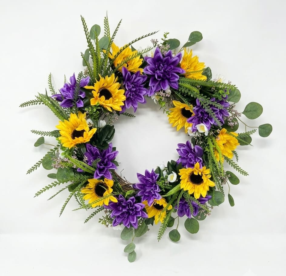 Sunflower Grapevine Wreath - Bright, cheerful sunflowers alternating with rich purple dahlia-like blooms create a high-contrast welcome with this sunflower grapevine wreath-perfect as a spring or summer door accent or everyday home décor. Designed for a recipient who loves vibrant color and a relaxed, natural look, it announces warmth and good cheer the moment someone approaches the home.  Made on an 18" grapevine wreath form, the design is full and layered: bold yellow sunflowers sit beside saturated purple dahlias with airy filler and eucalyptus-style greenery that extends slightly outward for a slightly wild, garden-fresh silhouette. The mixed color palette of yellow, purple and green gives great curb appeal and pairs well with rustic or contemporary entryways.  Ideal for gifting to someone who appreciates seasonal, decorative touches-whether celebrating a housewarming, birthday, or simply brightening a room this silk wreath requires no watering and keeps its color year-round. Hang it on a front door, over a mantel, or use as a cheerful wall accent; the 18" size makes it a versatile focal point for many spaces.