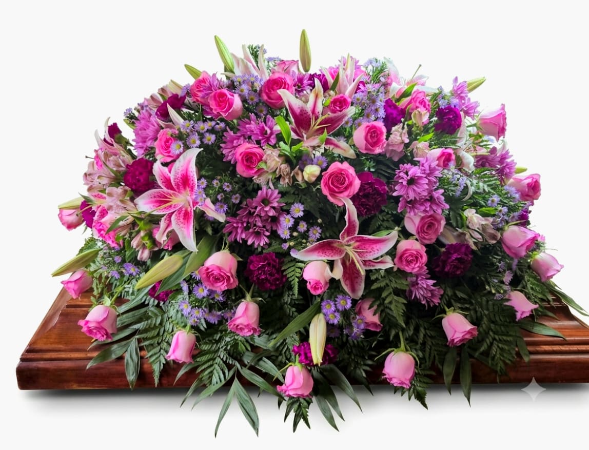 Stargazer Casket Spray - A lush cascade of pink roses and stargazer lilies drapes across a casket, creating a soft, farewell that reads as both comforting and dignified. This casket spray for sympathy and funeral services combines the drama of stargazer-style lilies with gentle lavender and purple accents to give the person you're honoring a beautifully layered, memorable tribute.  Carefully arranged with alstroemeria, carnations, daisies, chrysanthemums and roses, the composition is dense and full, spreading broadly with flowers that cascade toward the edges for an abundant, formal silhouette. The palette of pink, purple, lavender, white and green balances fragrant focal blooms with smaller daisy-like clusters and textured filler, providing visual depth from every viewing angle.  Choose this spray to convey love, respect, and remembrance for a funeral or memorial service-the kind of arrangement that helps the grieving feel seen and comforted. 