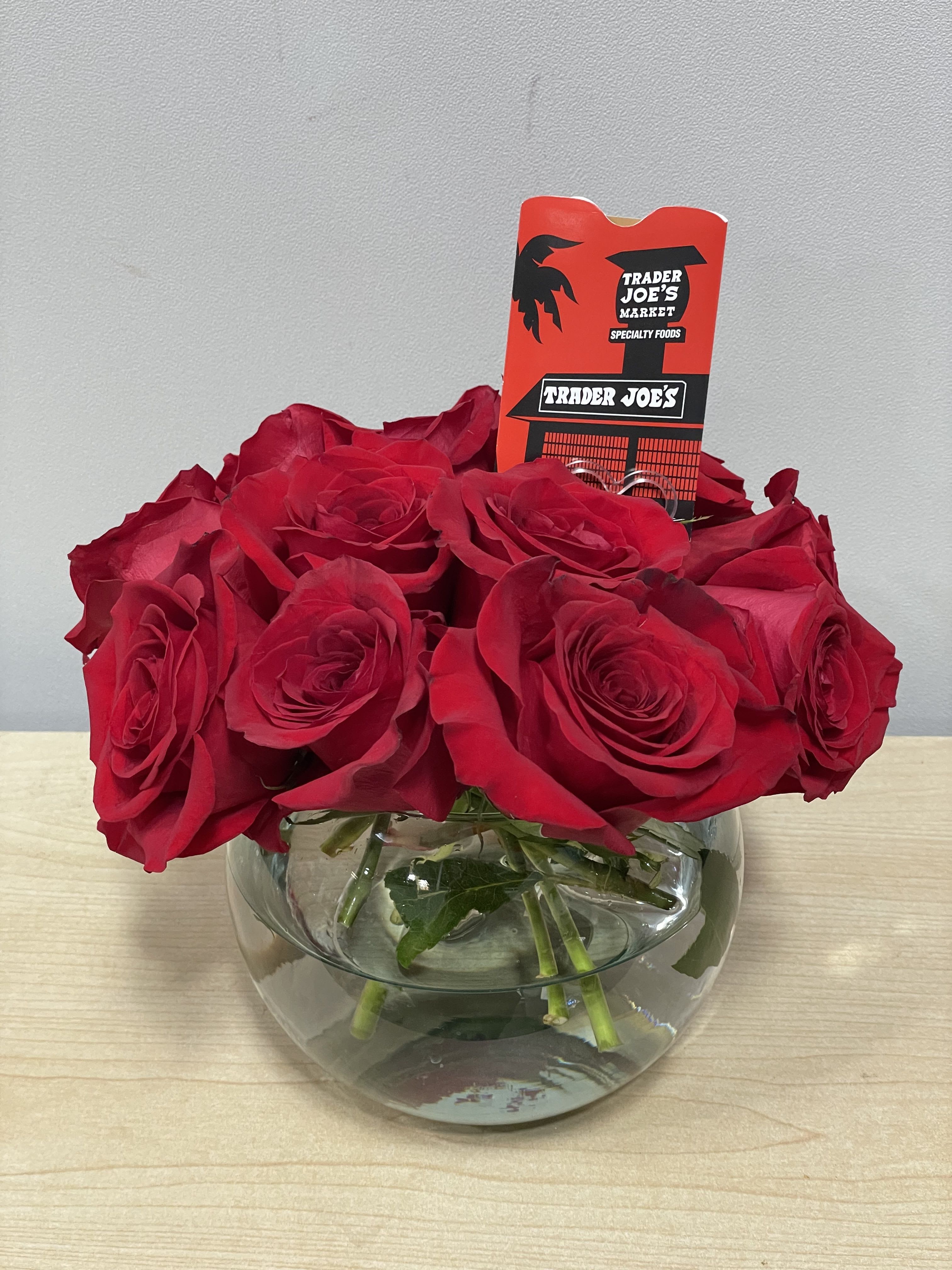 Red roses arranged in a round glass vase with a Trader Joe's tag